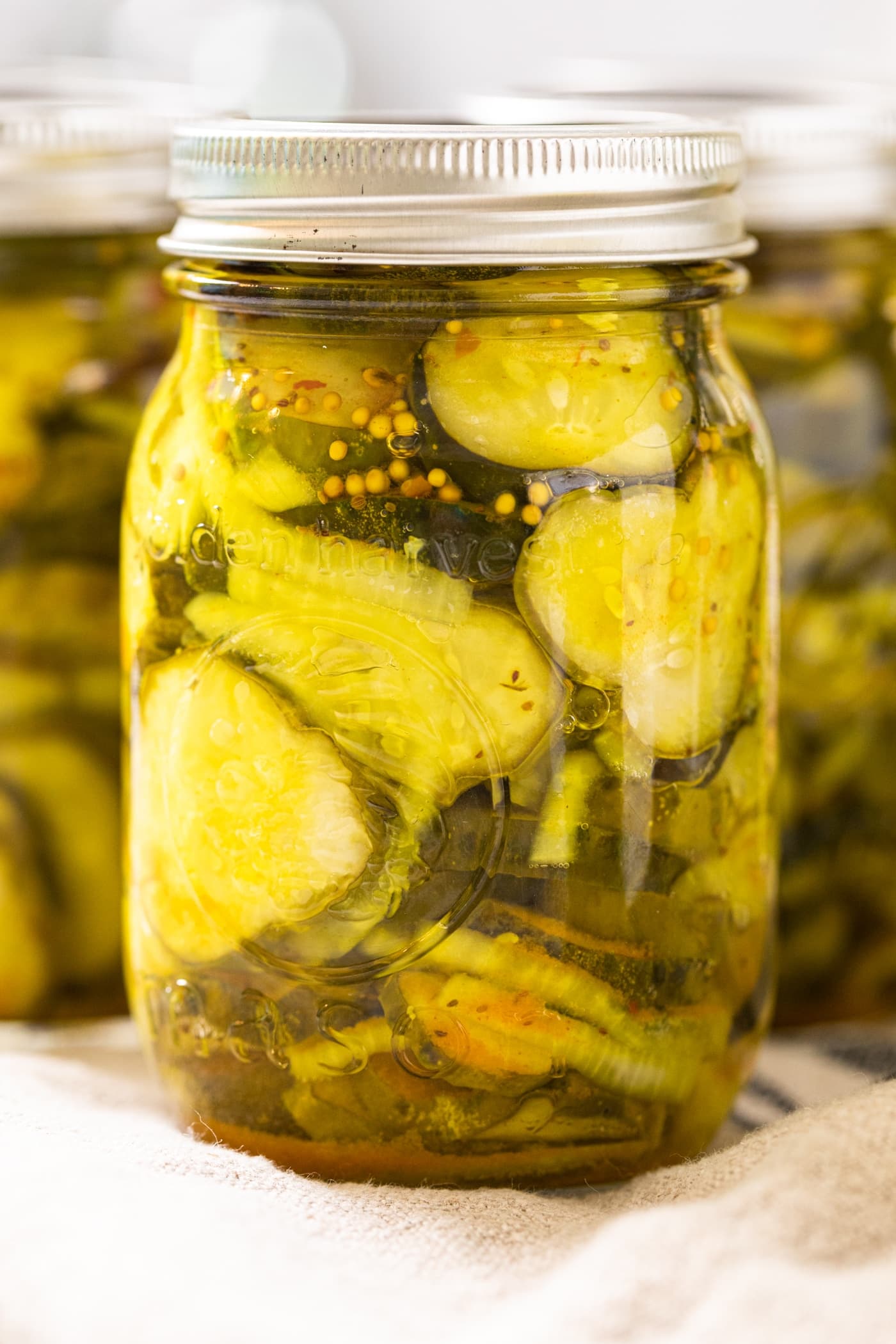 Very close up picture of glass jar filled with yellow and green colored bread and butter pickles sitting in brining liquid