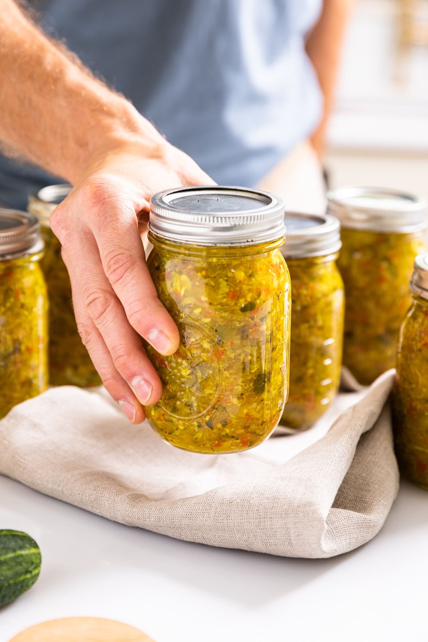 Hand holding glass jar filled with pickle relish with other filled jars in background