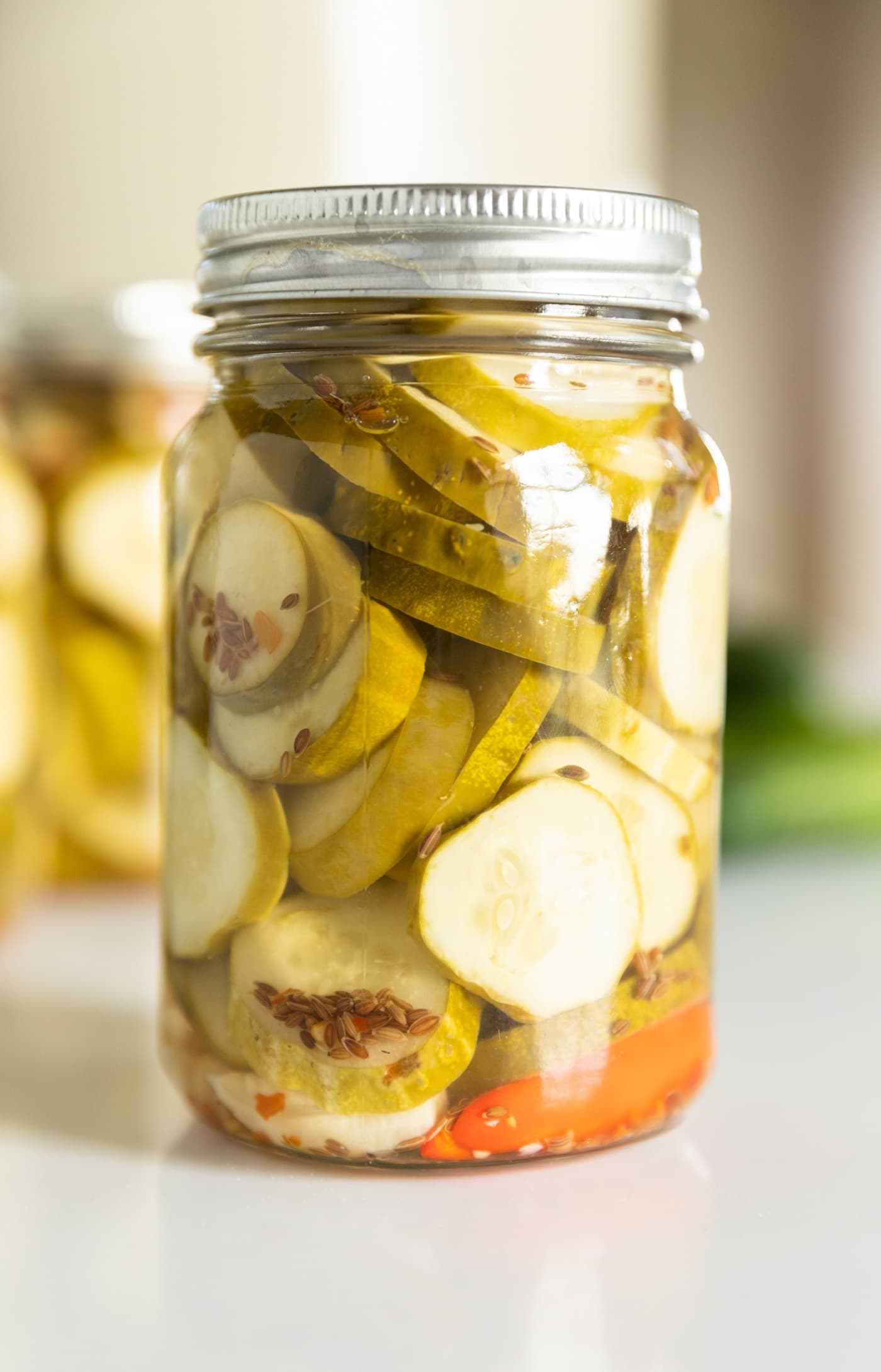 Close up view of glass canning jar filled with spicy dill pickles sitting on white countertop with other filled canning jars in background