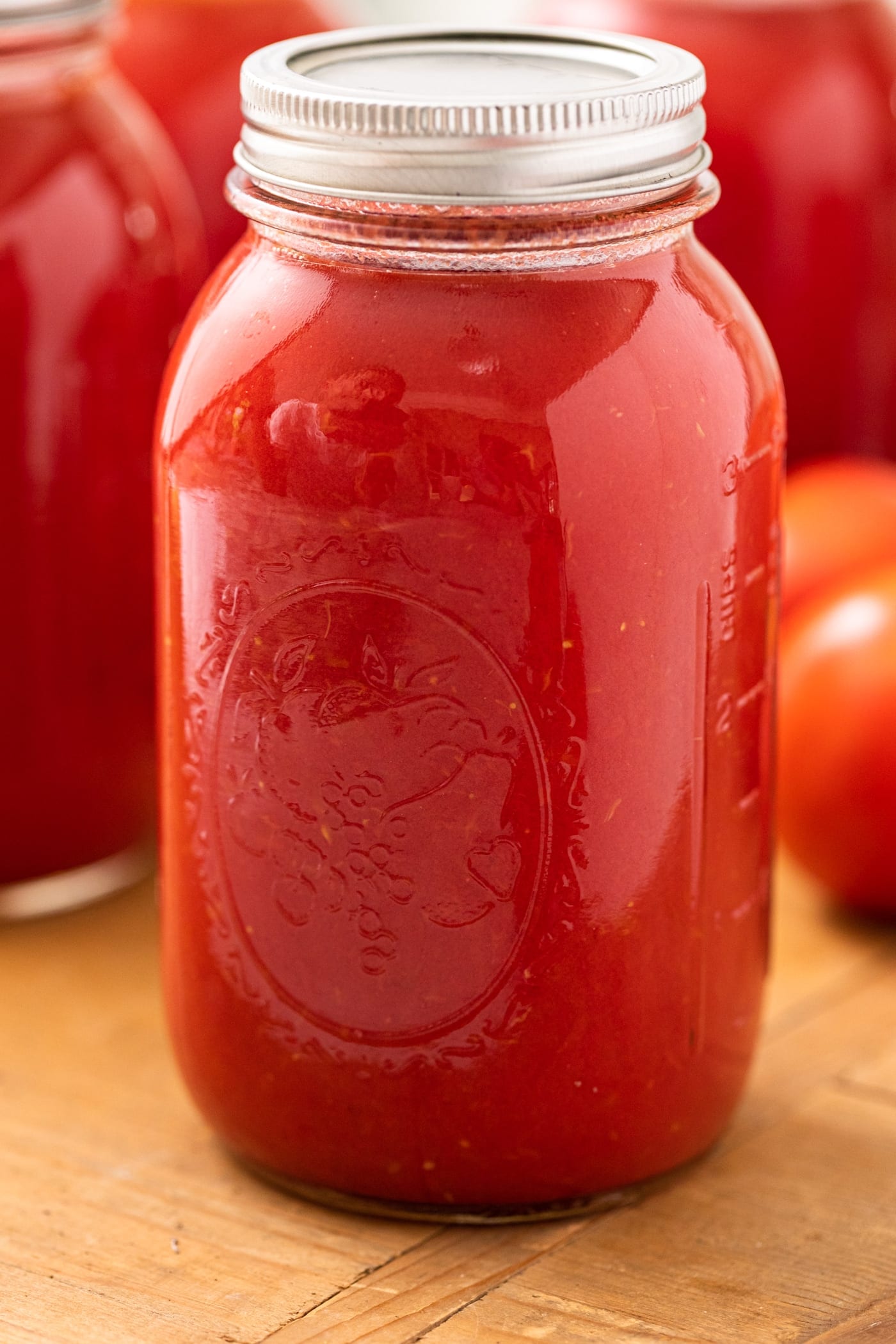 Glass jar filled with tomato juice with lid and ring on top sitting one wooden board