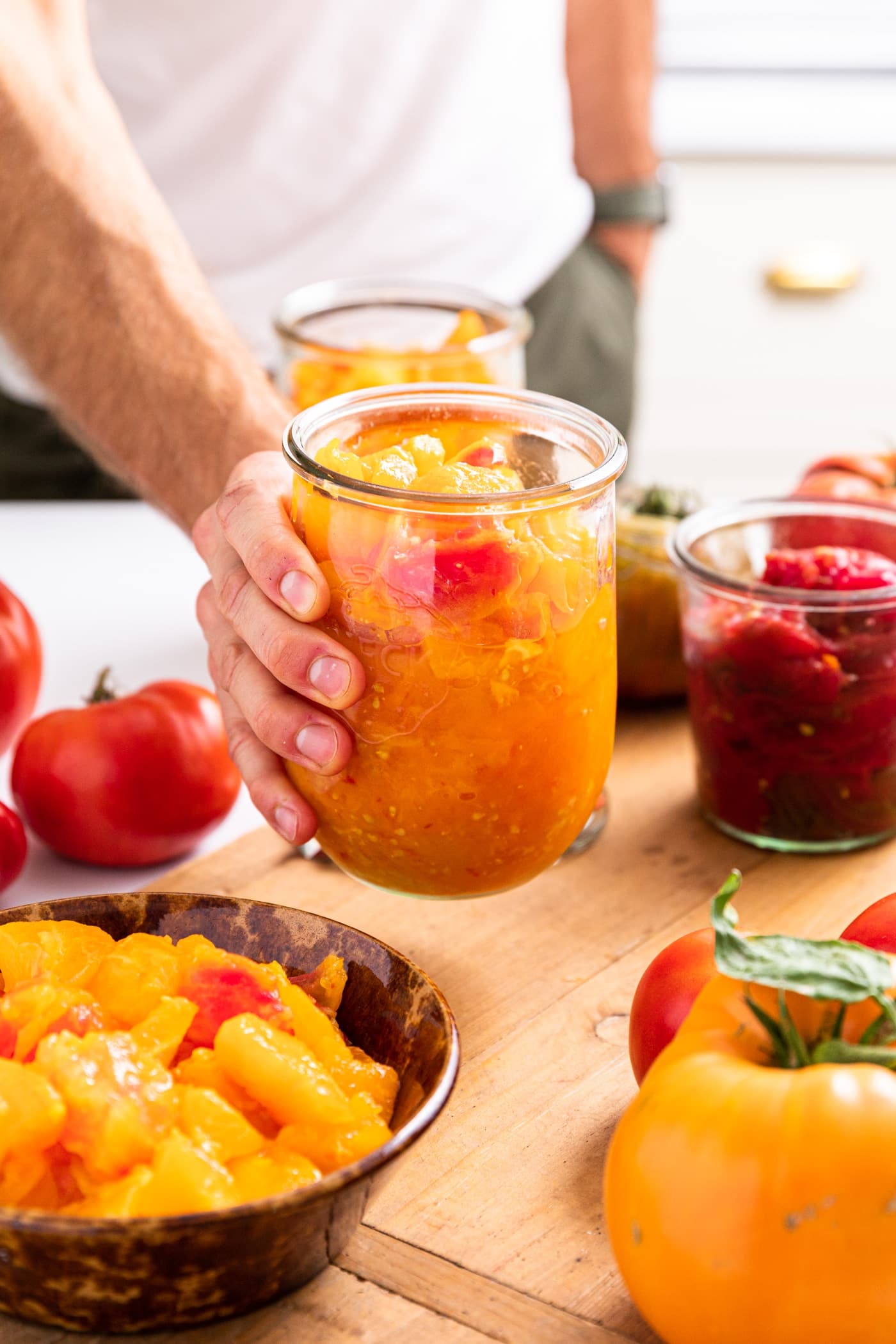 Hand holding glass container filled with red and yellow colored tomatoes all on wood board