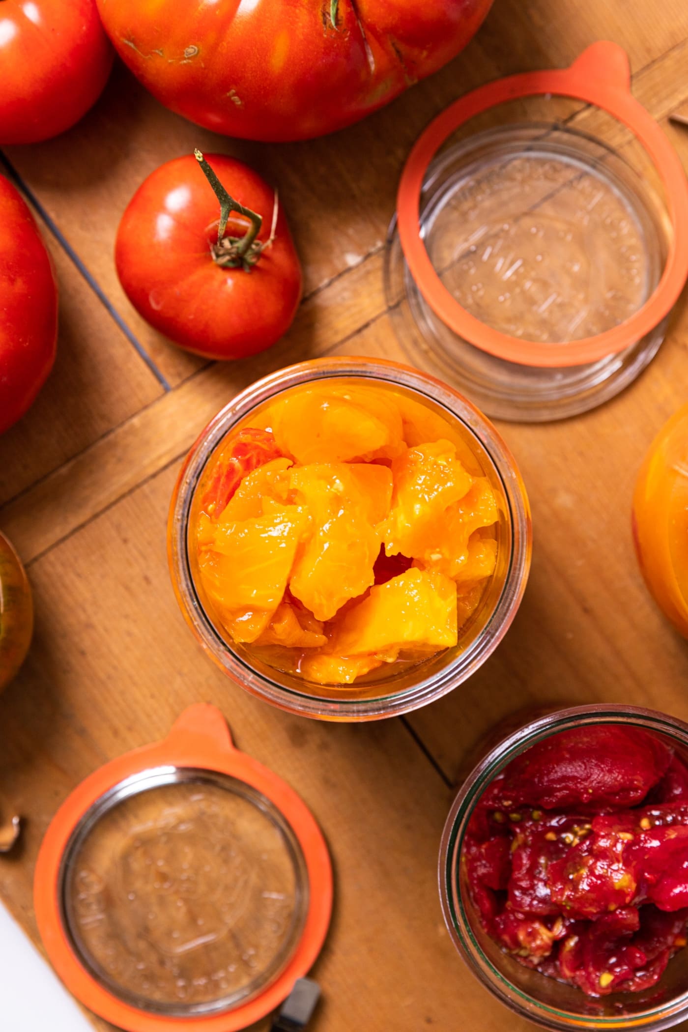 Top down view of yellow and orange colored tomatoes sitting in glass jar with extra tomatoes sitting around on wood board