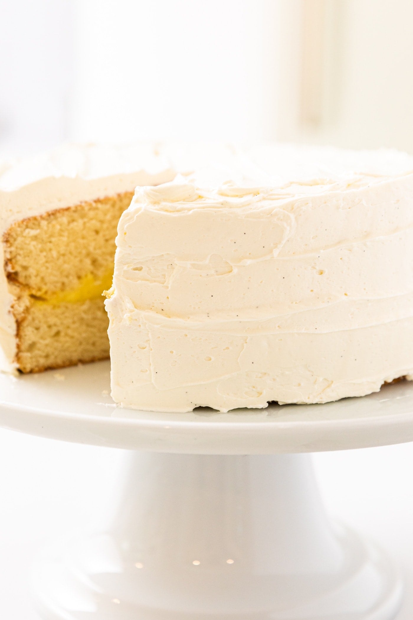 Side view of white frosting on white layer cake sitting on white cake plate