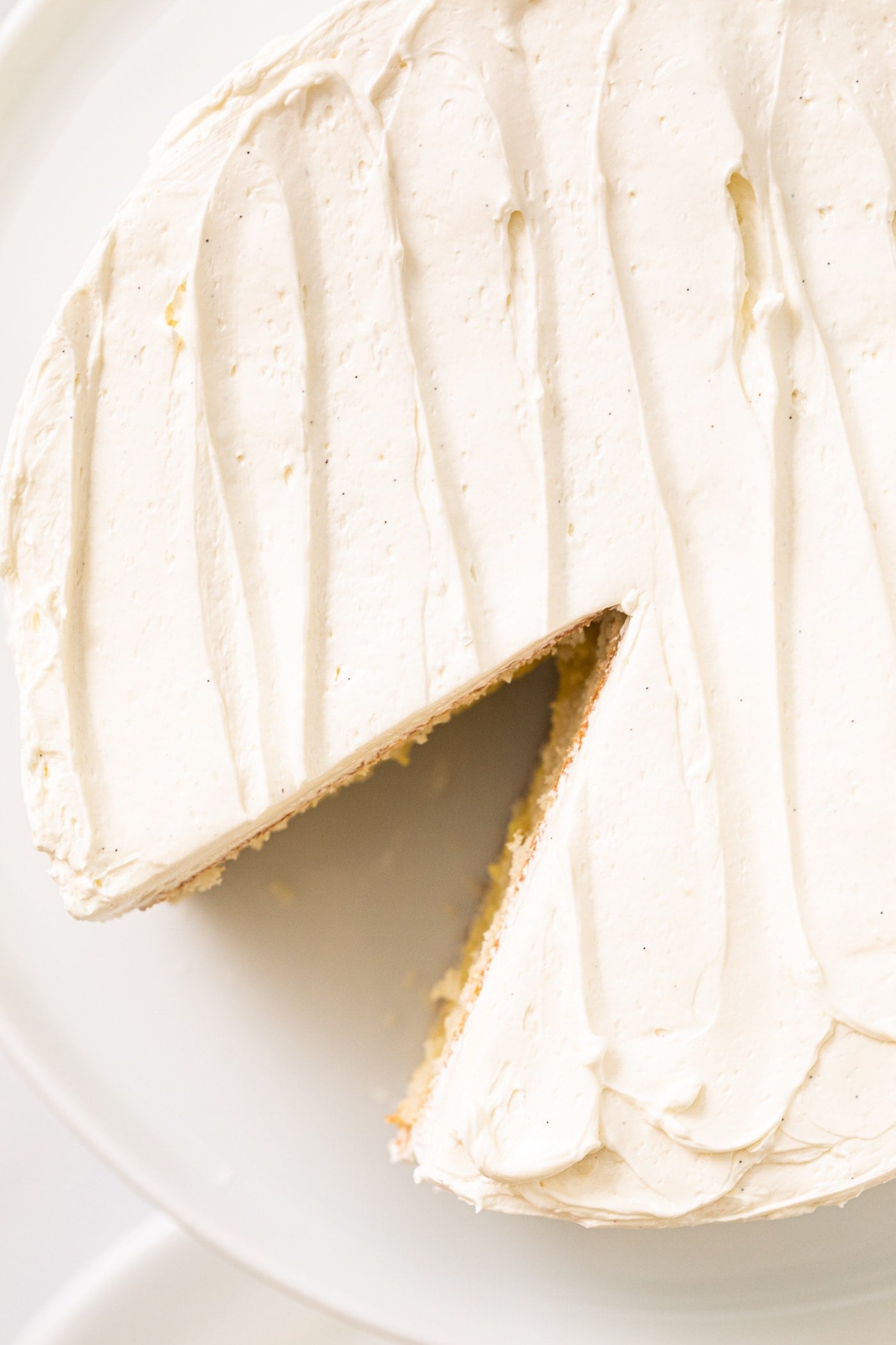 Top down view of white frosted cake with swirled effect on top sitting on white cake plate