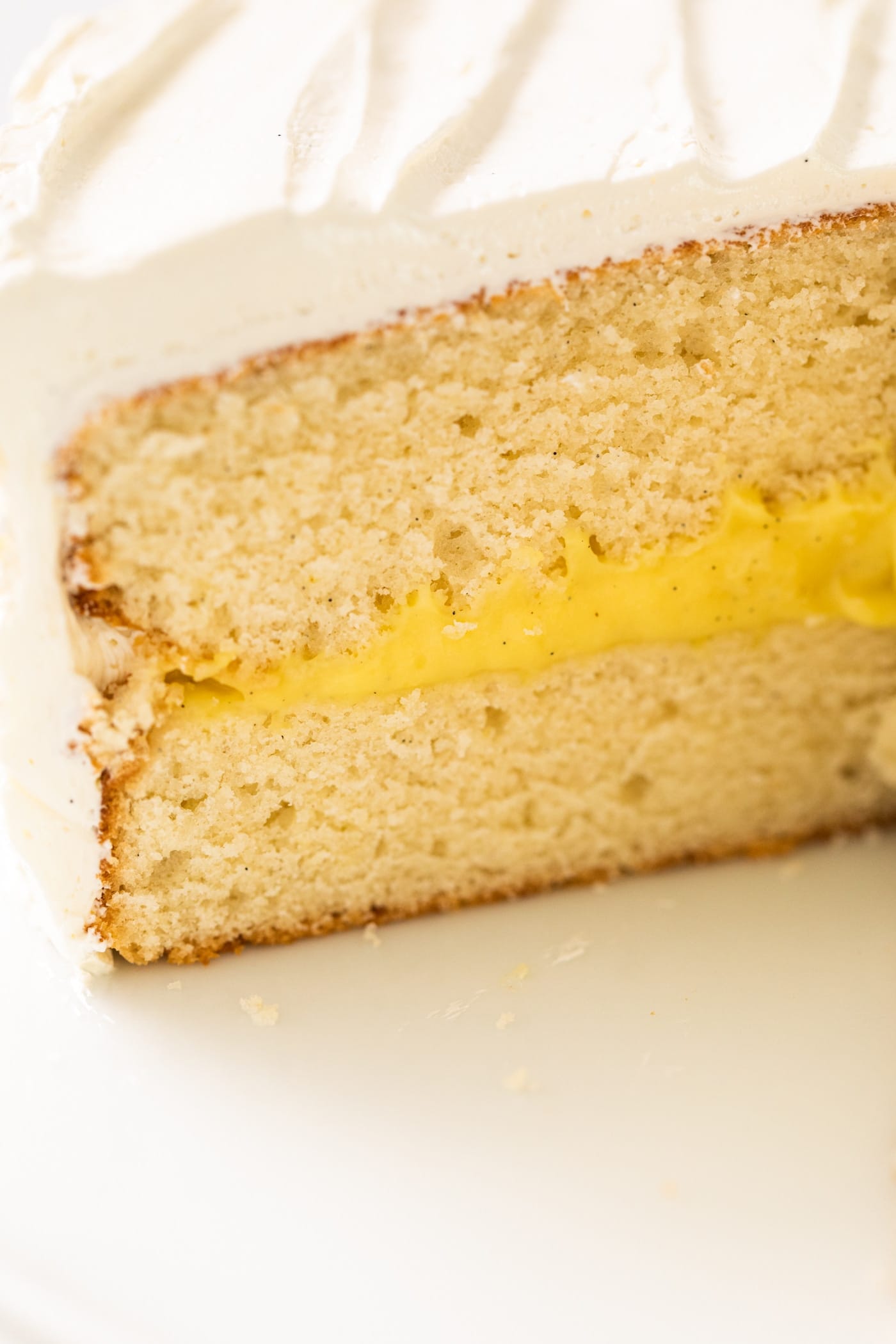 Side view of sliced section on white layer cake with yellow colored pudding filling in the middle of two layers of white cake sitting on white cake plate