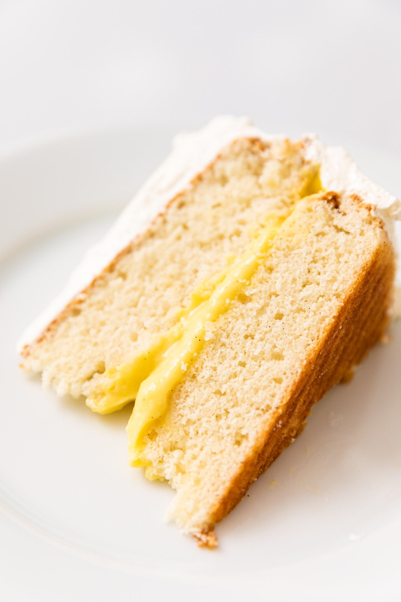 Close up view of slice of white cake with yellow layer of pudding filling sitting on white plate with white frosting
