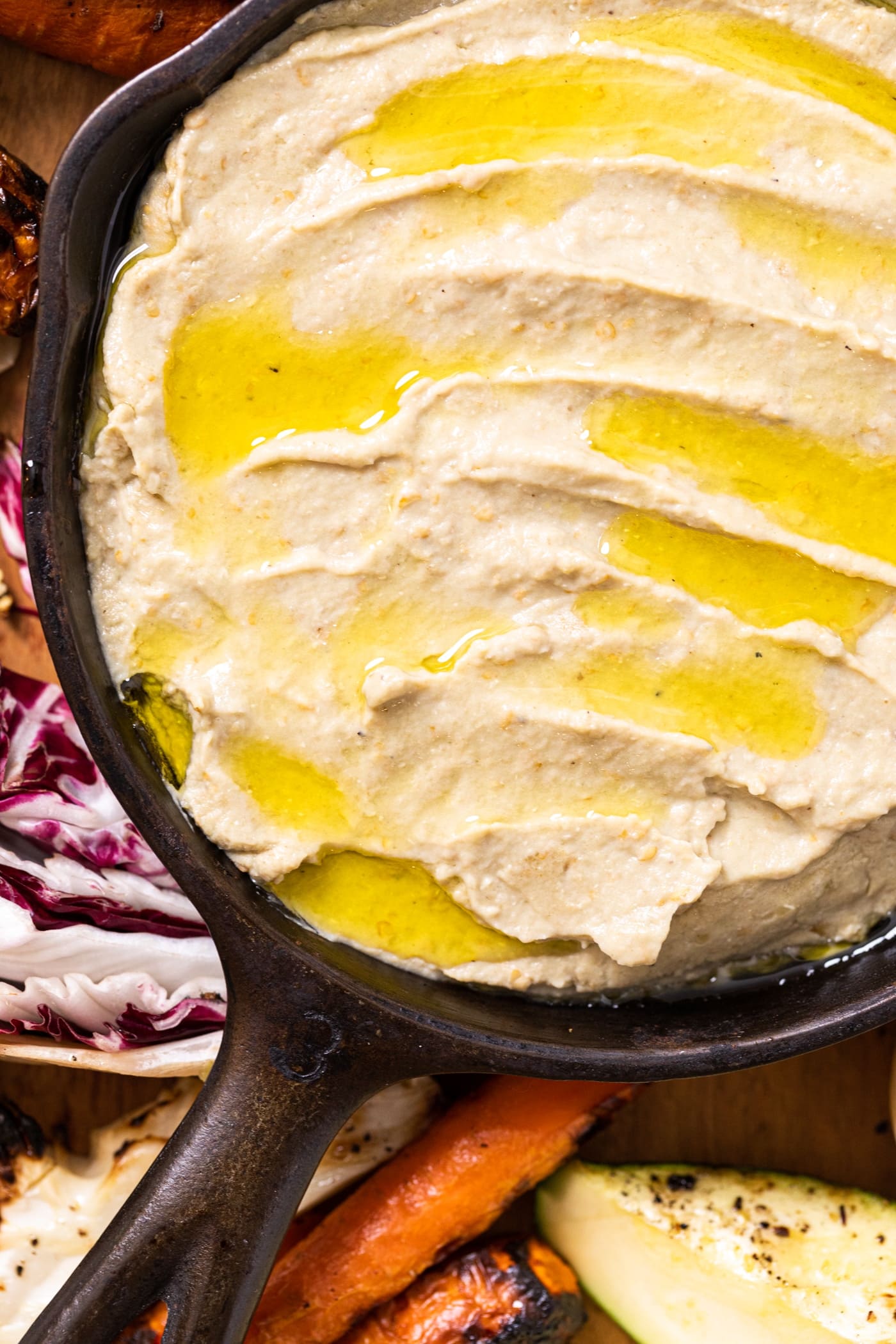 Close up top down view of Baba ganoush in black cast iron skillet with olive oil all over the top with grilled vegetables around