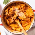 Top down view of large kettle sitting on white countertop filled with orange colored squash pasta with wooden spoon inside