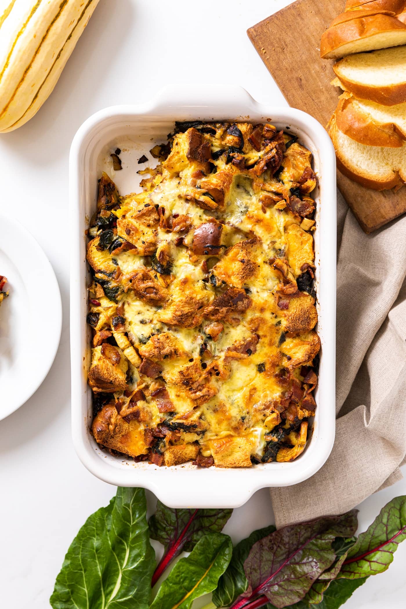 Top down view of white casserole dish sitting on white countertop filled with brown colored egg strata with slices of bread on the side