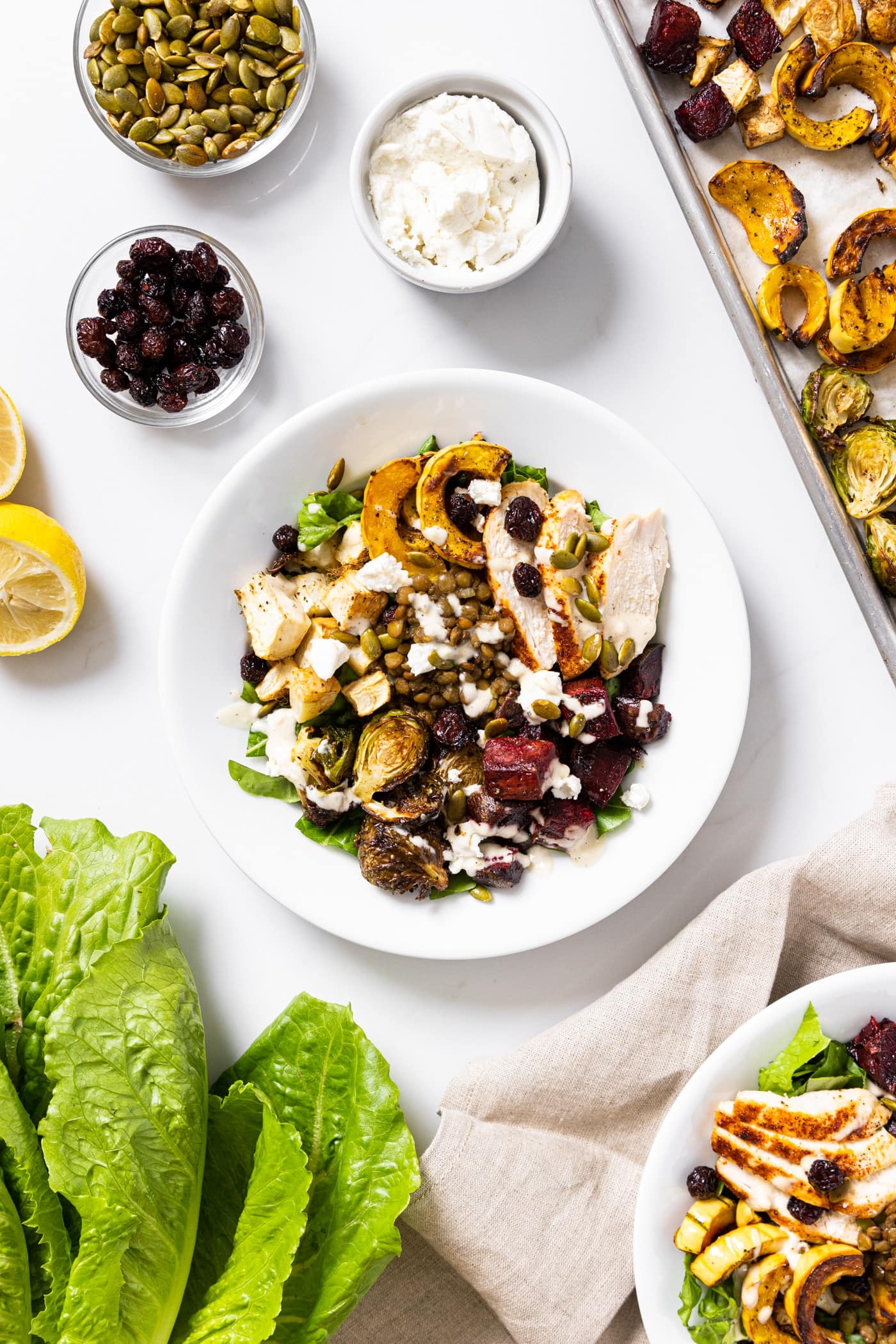 Far away top down view of white bowl surrounded by ingredients in this harvest bowl all sitting on white countertop with green lettuce to the side