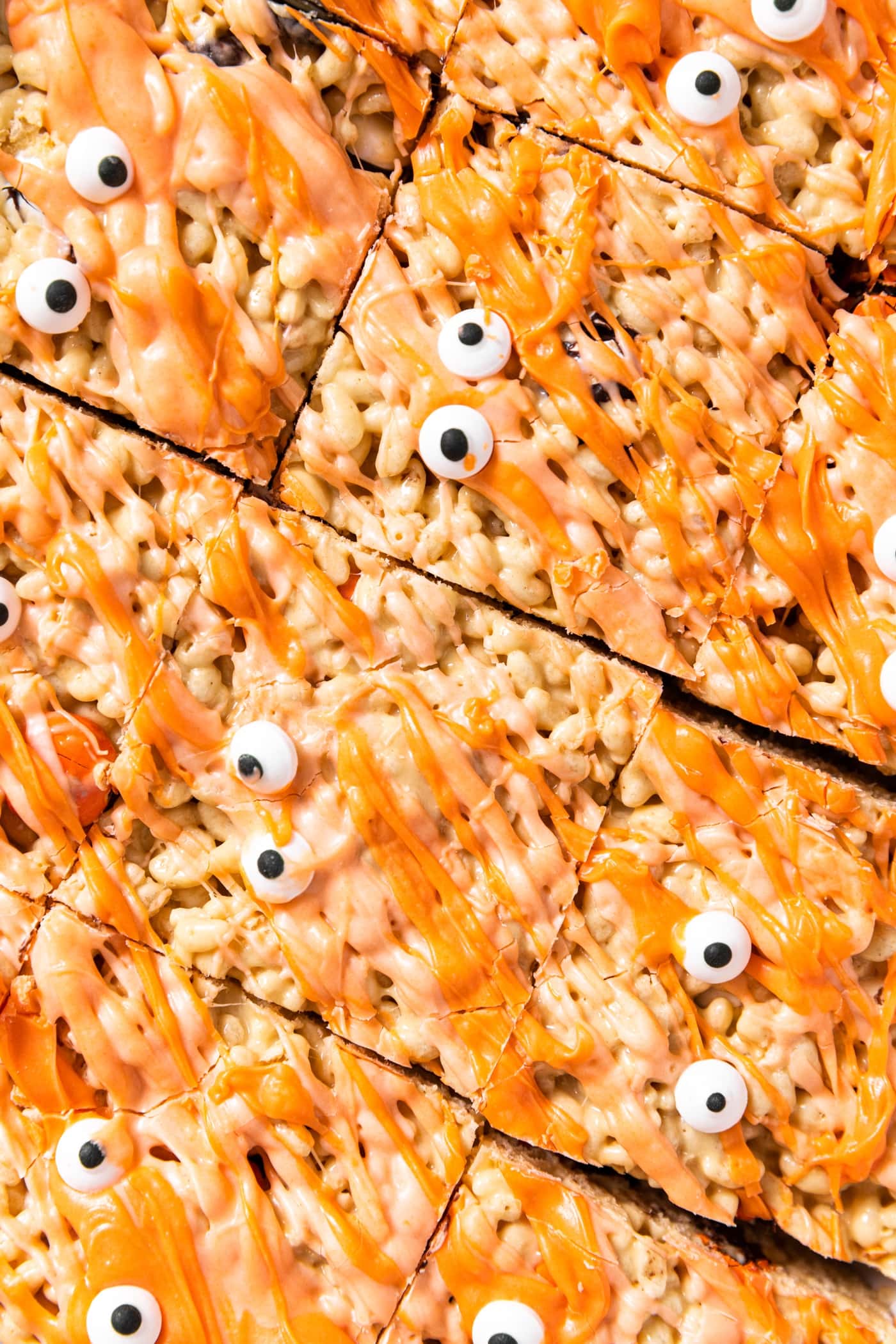 Top down view of Rice Krispies cut into squares and drizzled with orange white chocolate with little edible white eyeballs