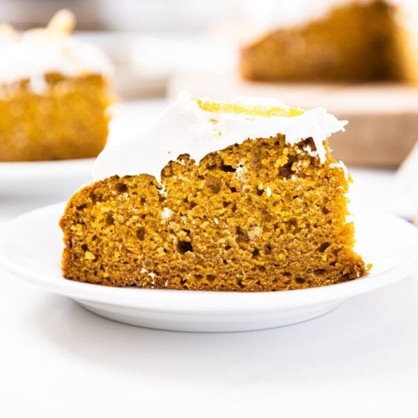 Large slice of pumpkin cake sitting on white plate with other slices of cake in background all on white countertop