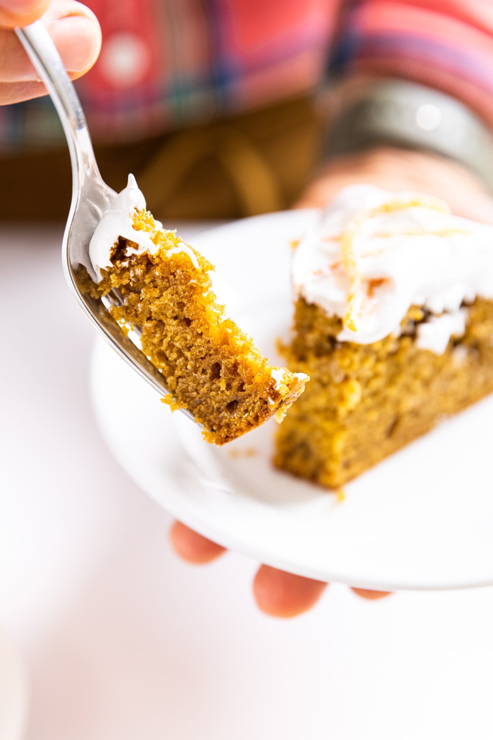 Hand holding fork bite of pumpkin applesauce cake with hand holding other part of cake