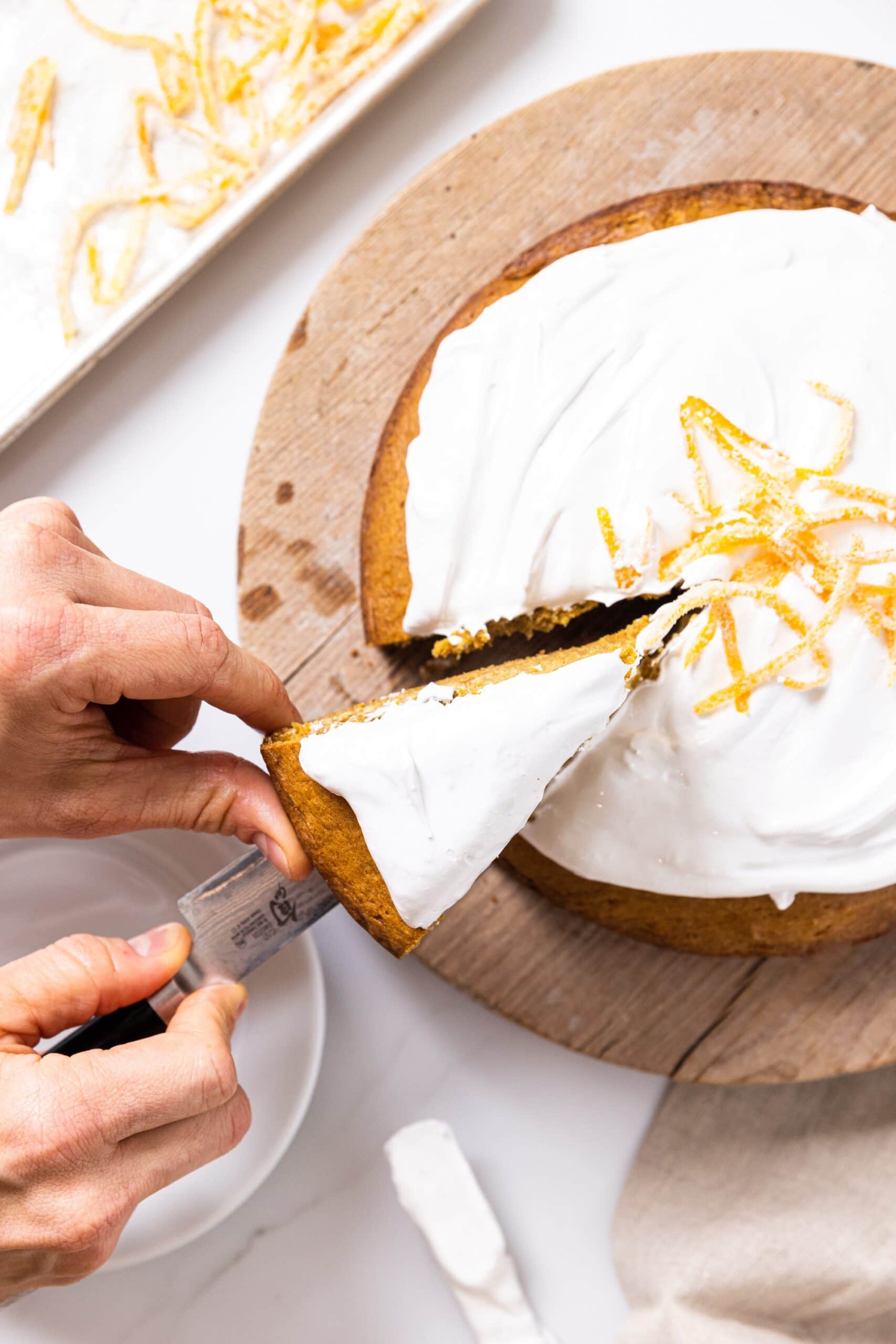 Top down view of hand taking slice of pumpkin cake with white whipped topping out of rest of cake
