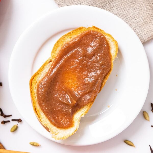 Top down view of white plate with slice of bread sitting on top with slathered brown pear butter one top with extra pears and spices on white countertop