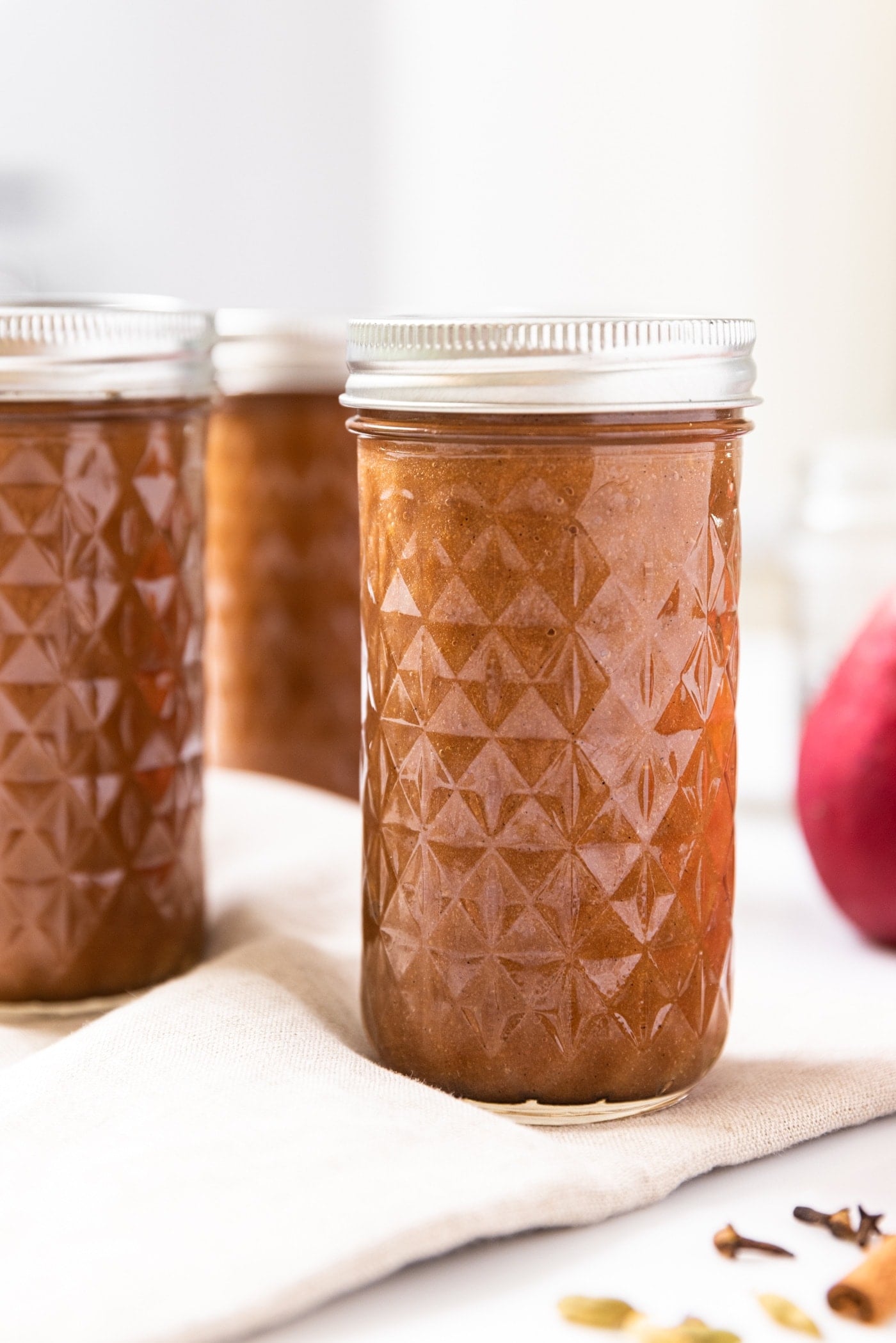 Narrow tall glass jar with diamond design filled with brown colored pear butter after being in the canner sitting on white countertop