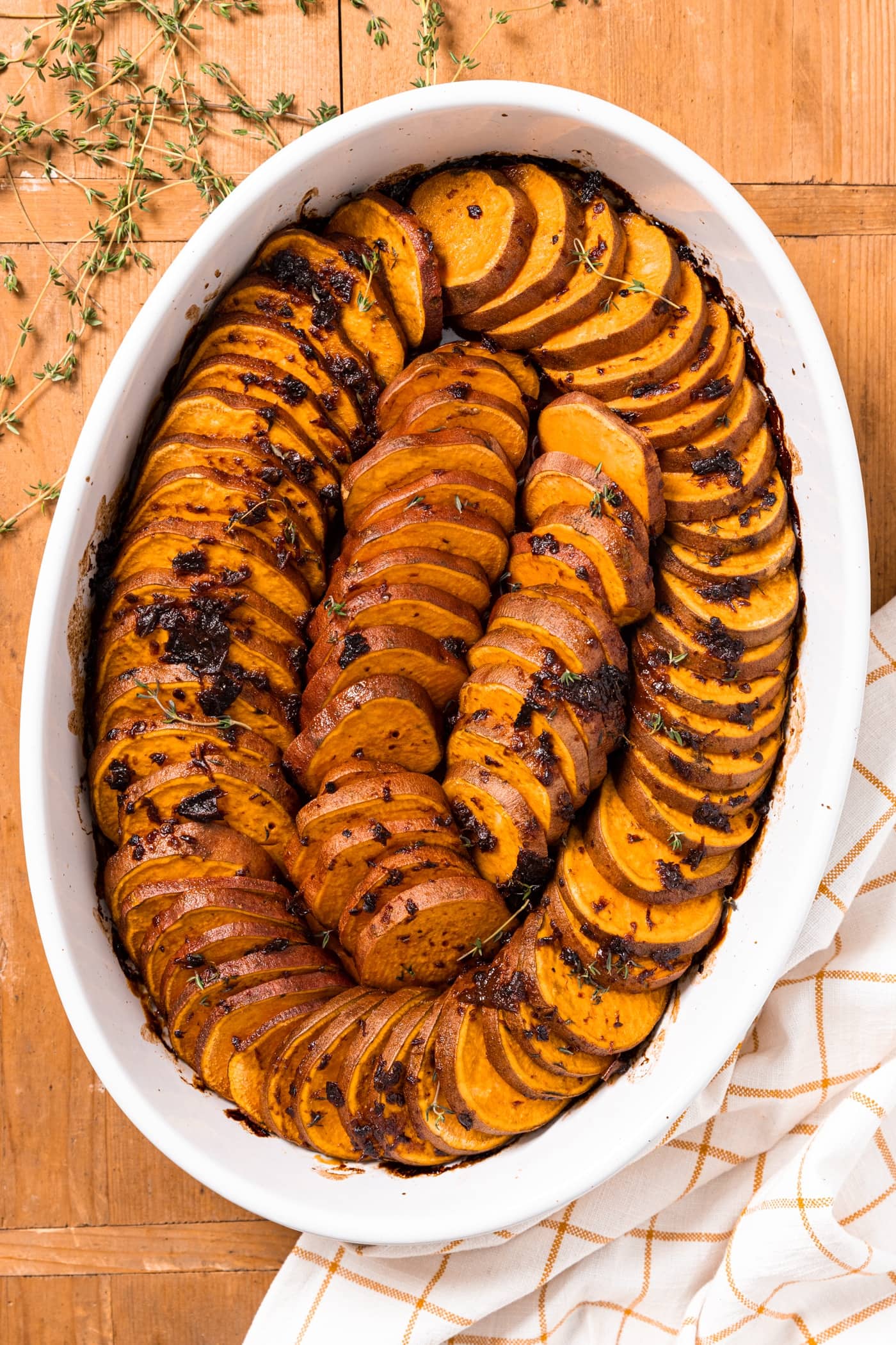 Top down view of white serving platter filled with shingled slices of sweet potato with chipotle butter poured over the top sitting on a wood board