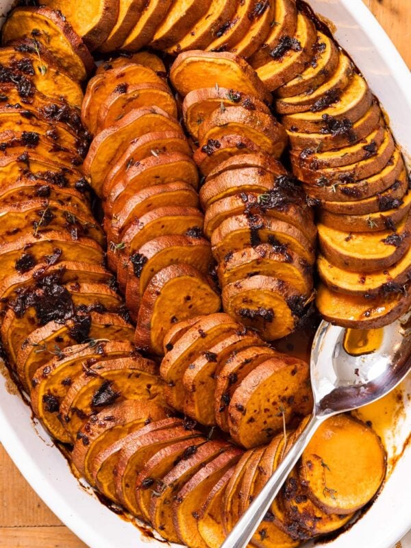 Top down view of white pan filled with slices of sweet potatoes topped with chipotle butter with spoon scooping out some