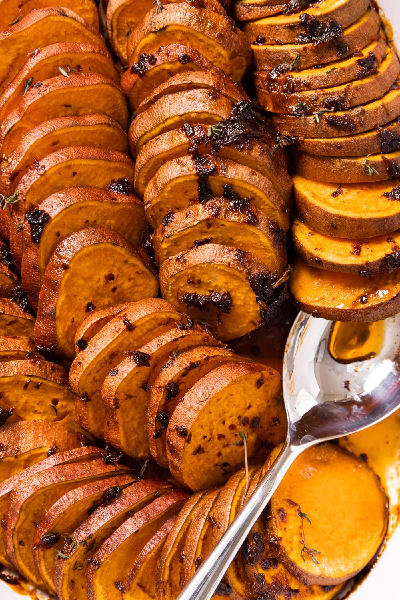 Top down view of sliced sweet potatoes sitting in baking dish with spoon scooping one of the potatoes
