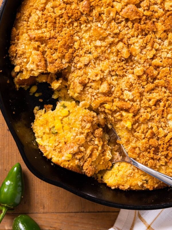 Top down view of black cast iron skillet sitting on wooden board filled with brown colored spoon bread mixture