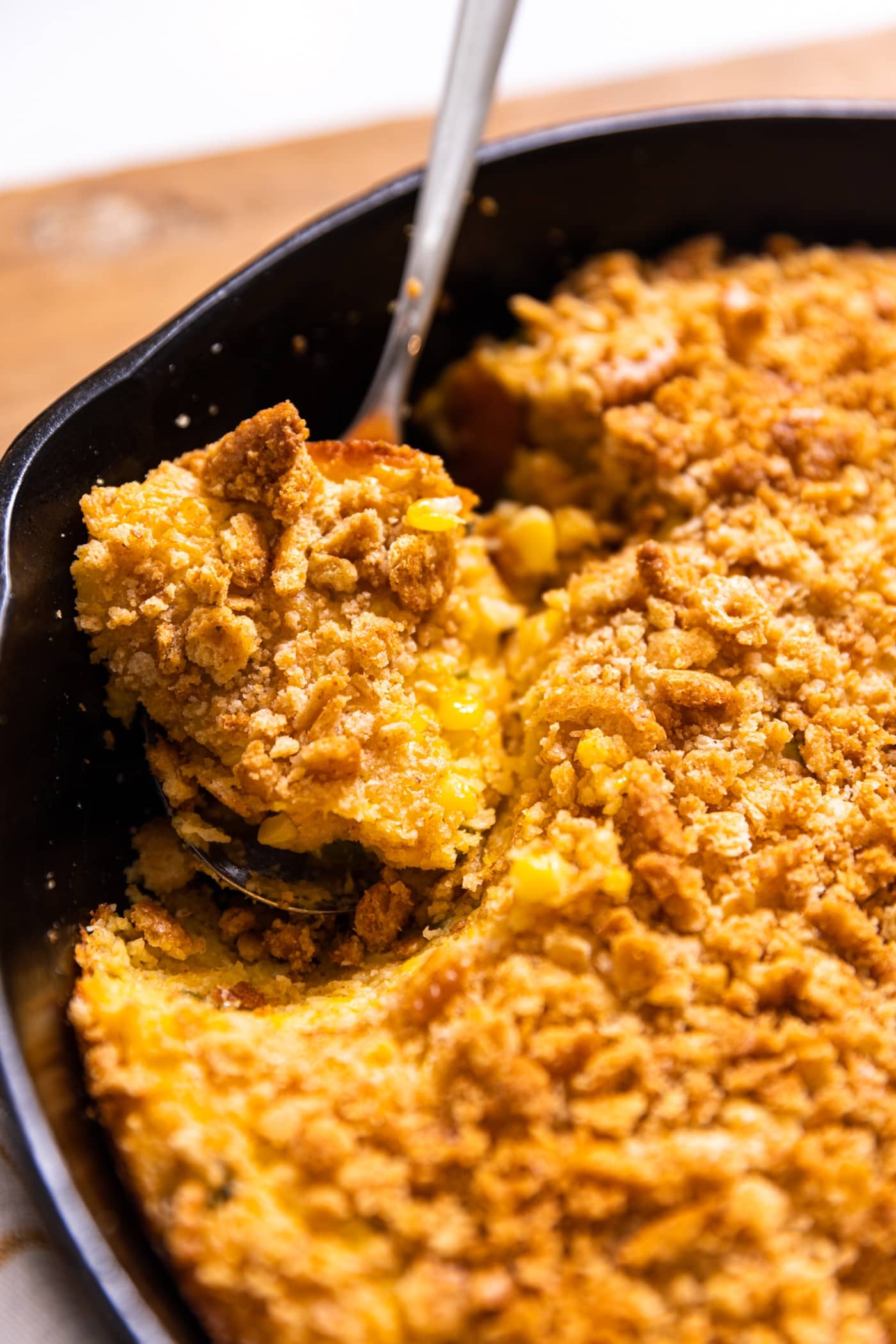 Side of large cast iron skillet filled with golden colored casserole with spoonful being scooped out