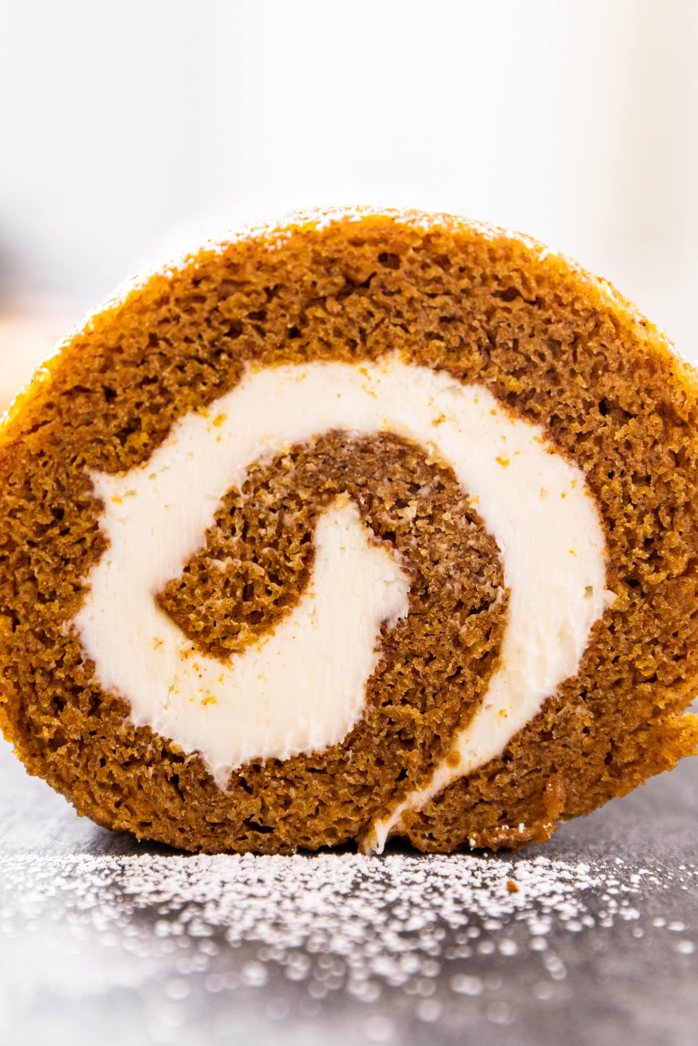 Side profile view of rolled pumpkin cake with cream cheese frosting sitting on piece of slate