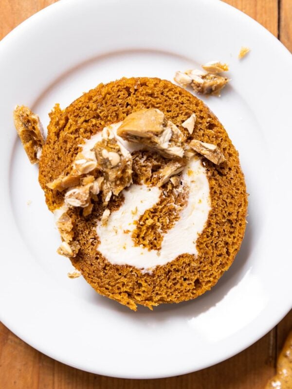 Top down view of white plate with slice of pumpkin roll on top with brittle sprinkled on top