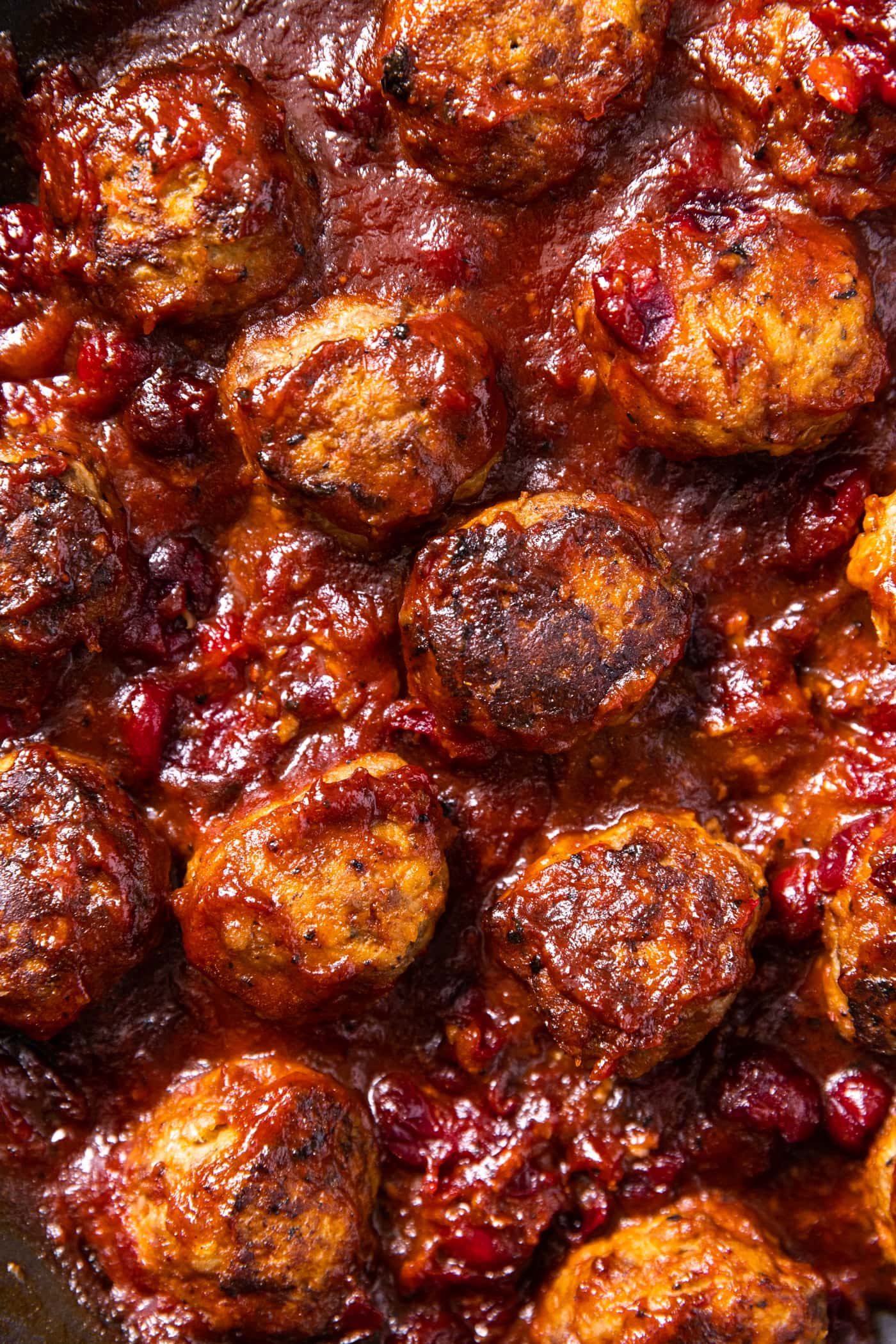 Top down close up view of cranberry sauce covered meatballs sitting in dark maroon sauce in skillet