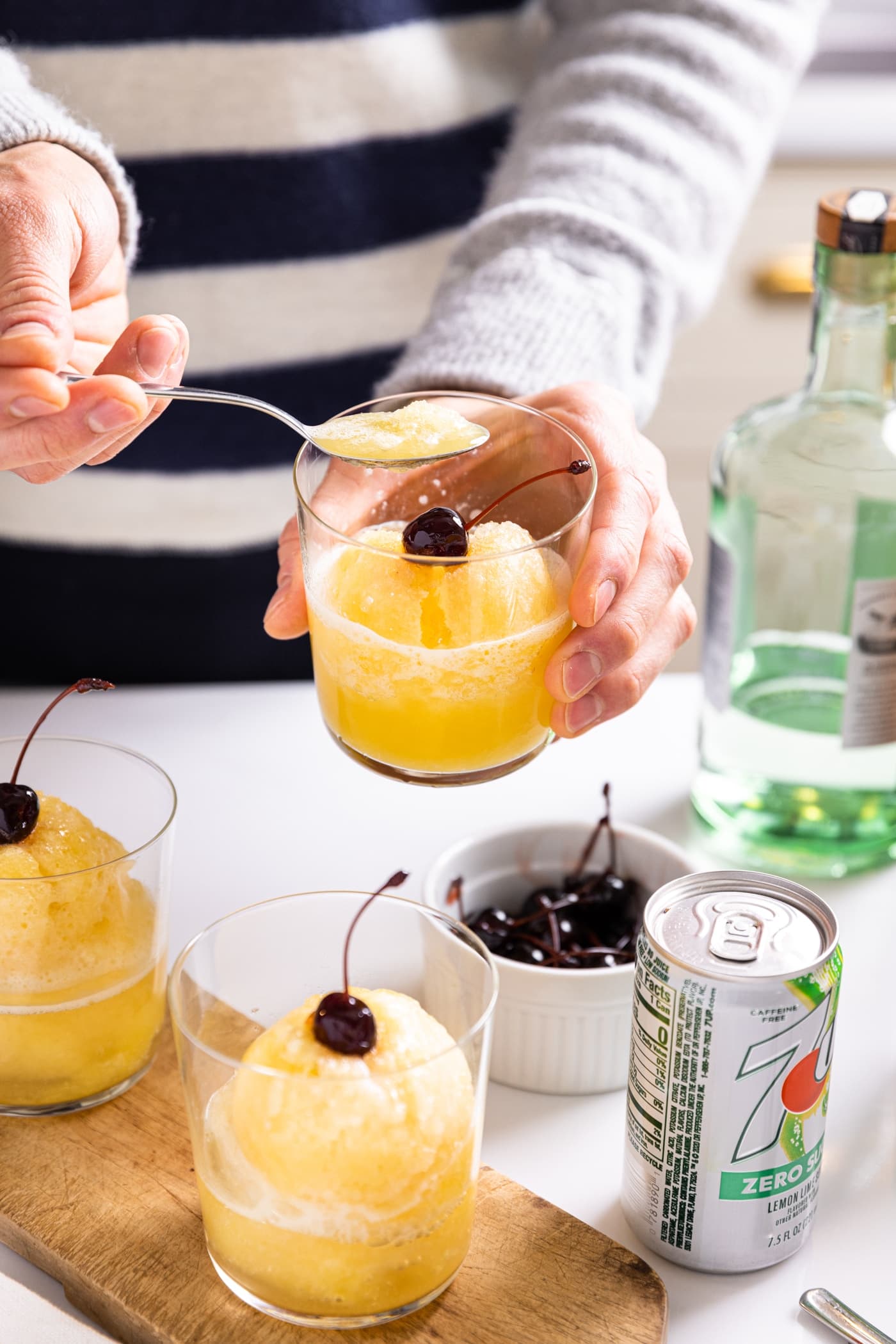Hand holding clear glass filled with yellow colored pineapple slush with spoon taking bite out of mixture