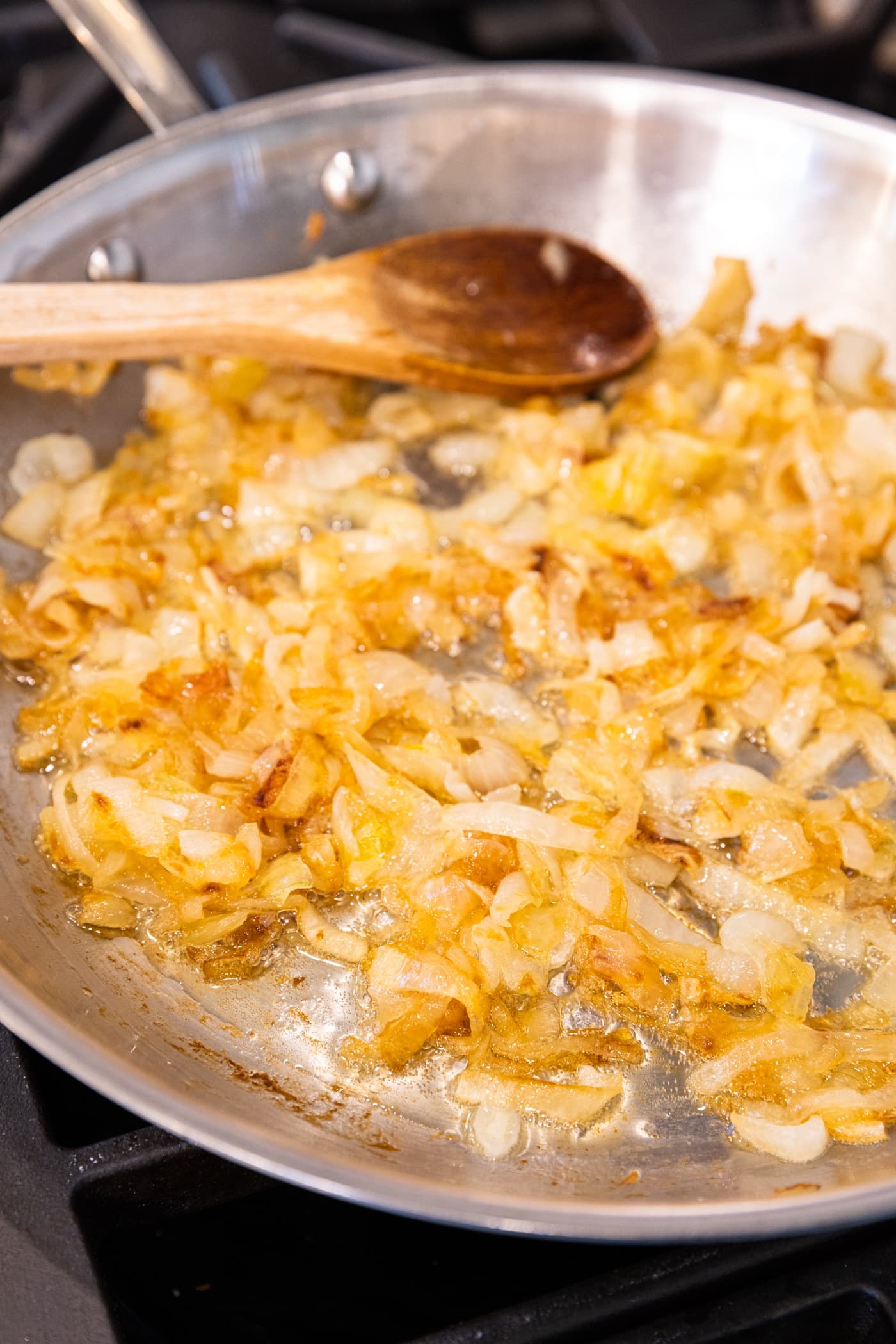Caramelized onions sitting in metal skillet sitting on flame with wooden spoon in background