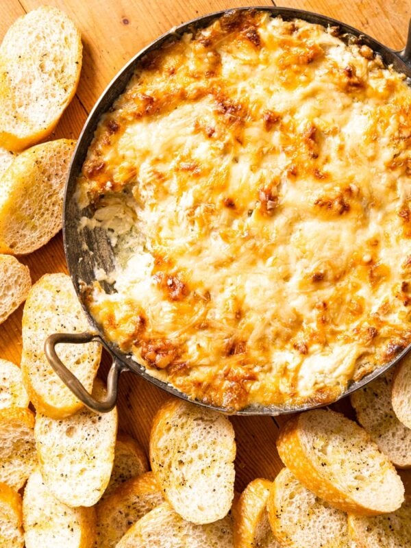 Top down view of copper pot filled with brown crusted cheese that was broiled in the oven sitting on wood board