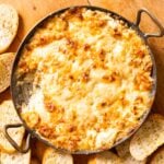Top down view of round copper pot with handles filled with browned cheese with pieces of bread sitting all around on wood board