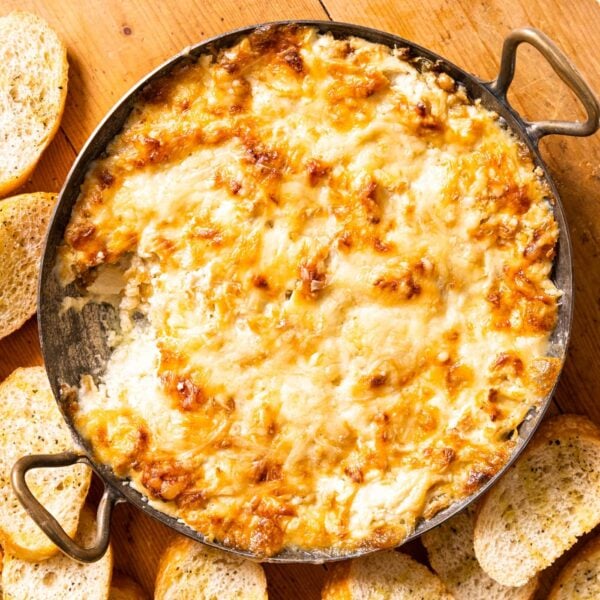 Top down view of round copper pot with handles filled with browned cheese with pieces of bread sitting all around on wood board