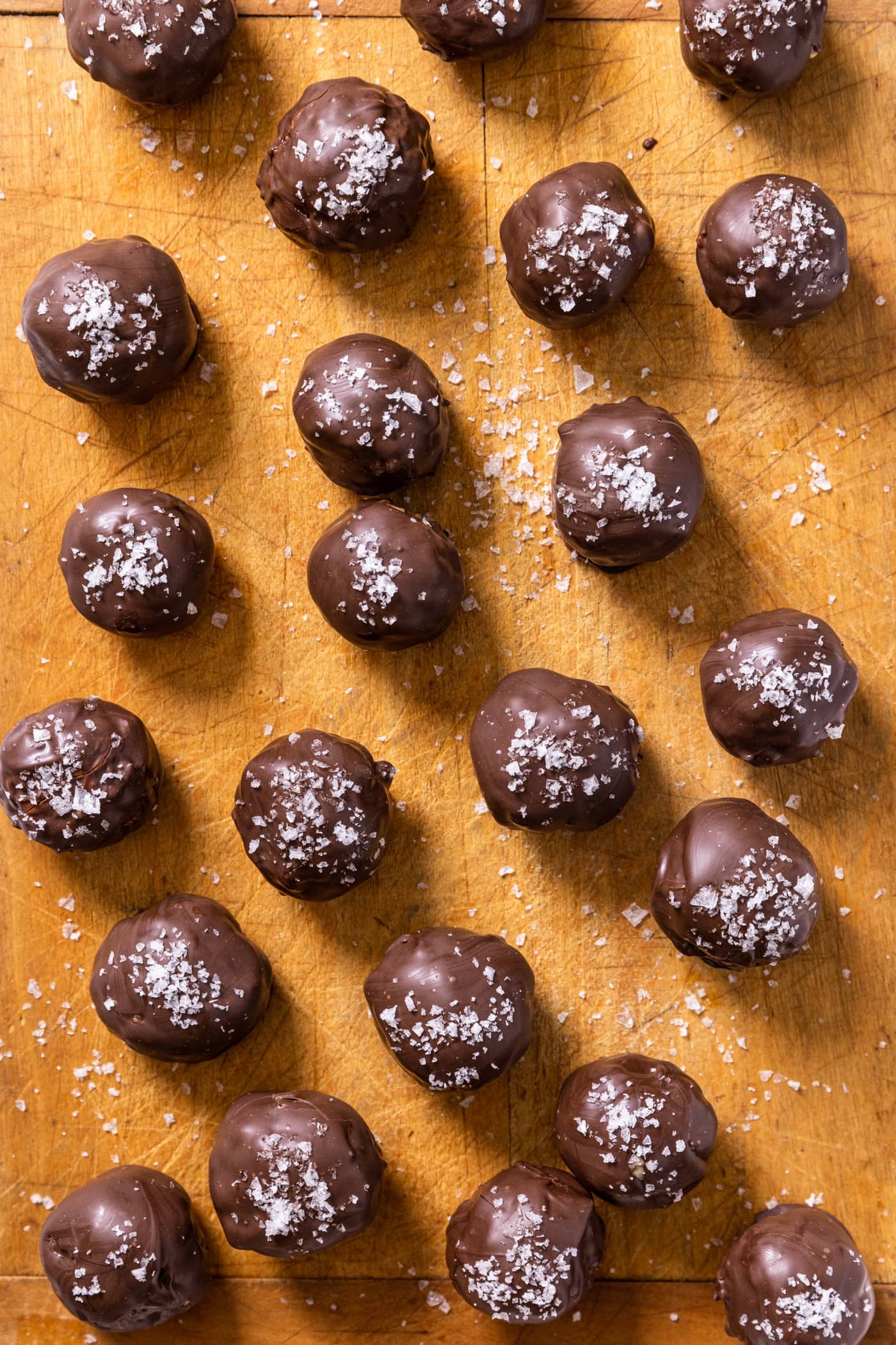 Top down view of chocolate peanut butter balls with sea salt flaked on top all on wood board