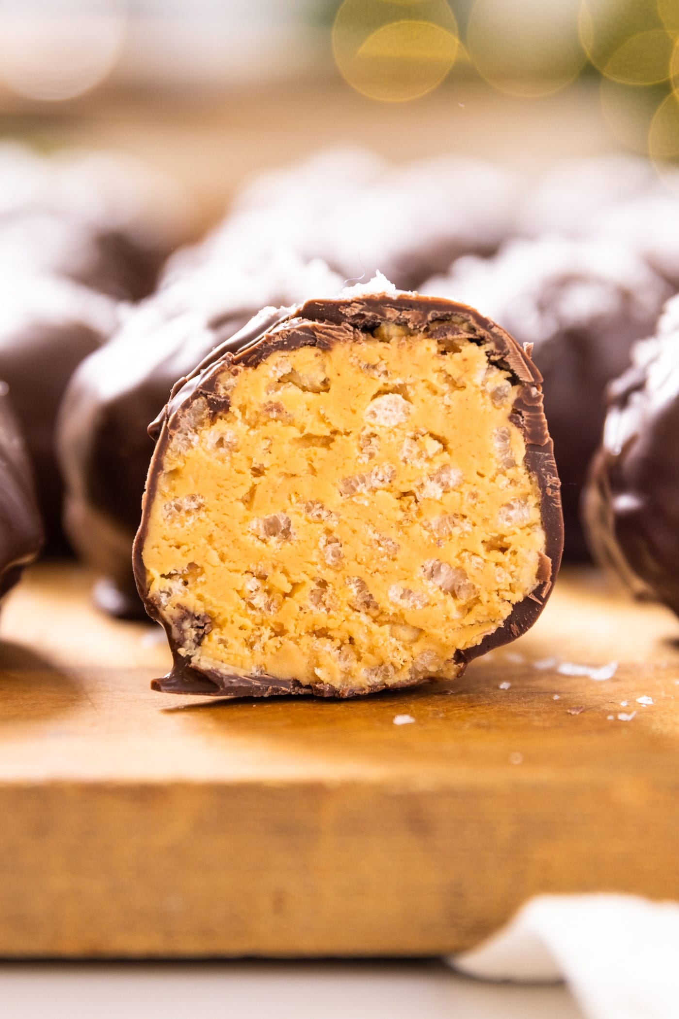 Peanut butter ball covered in chocolate cut in half and sitting on wood cutting board with other peanut butter balls all around