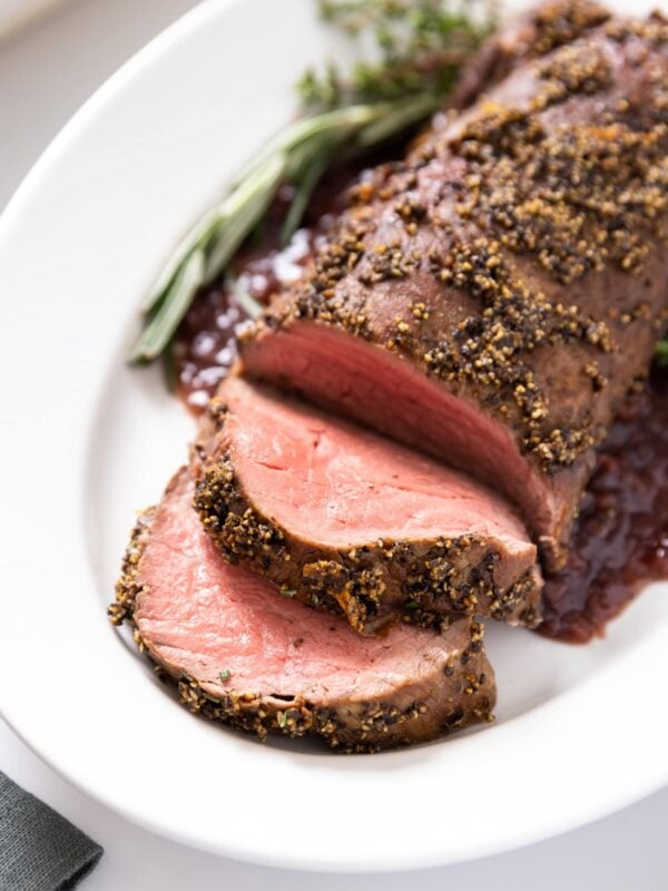Large white platter with beef tenderloin sitting on top with two slices laying over all on white surface