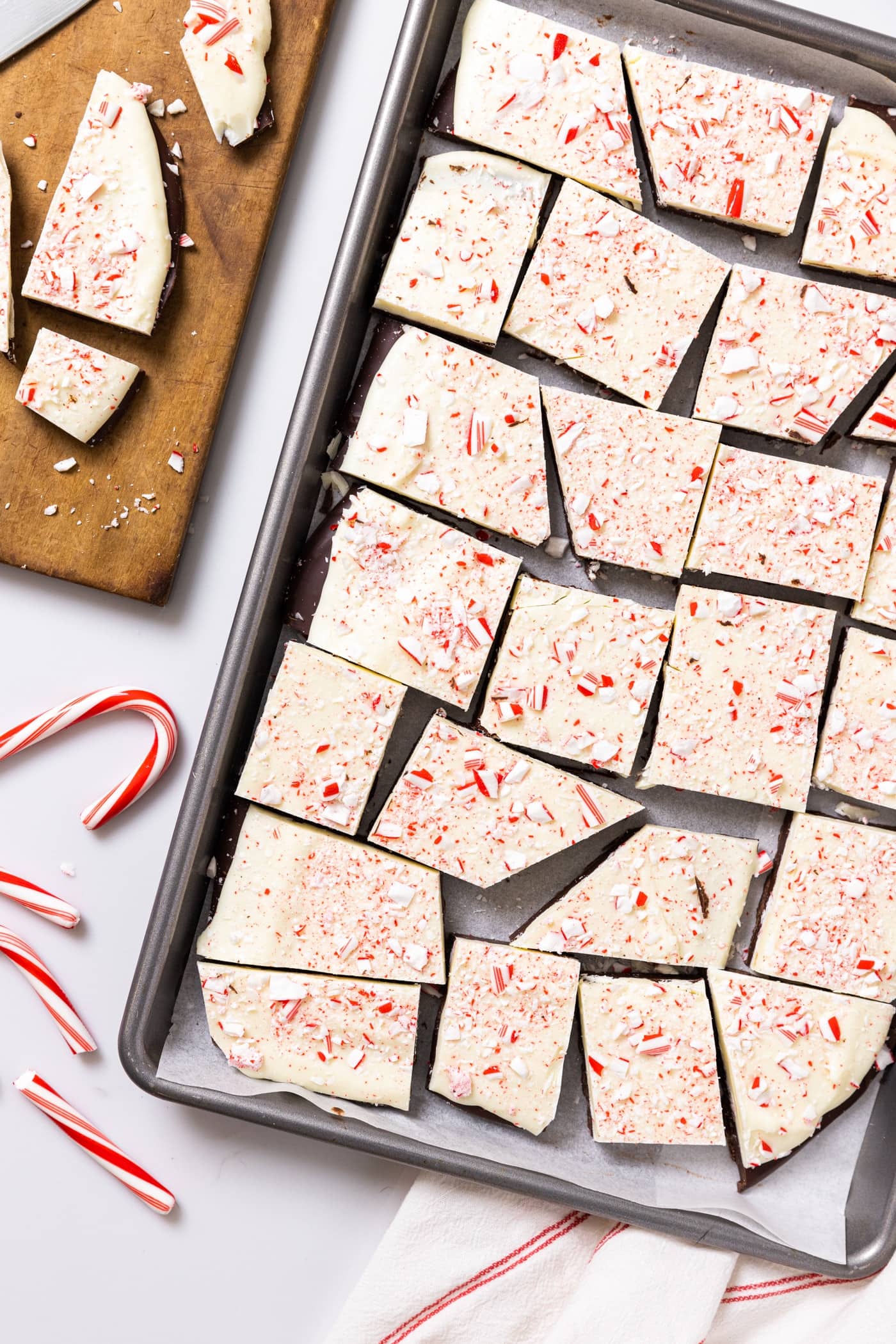 Top down view of metal baking sheet filled with uneven pieces of peppermint bark topped with pieces of crushed peppermint on white countertop