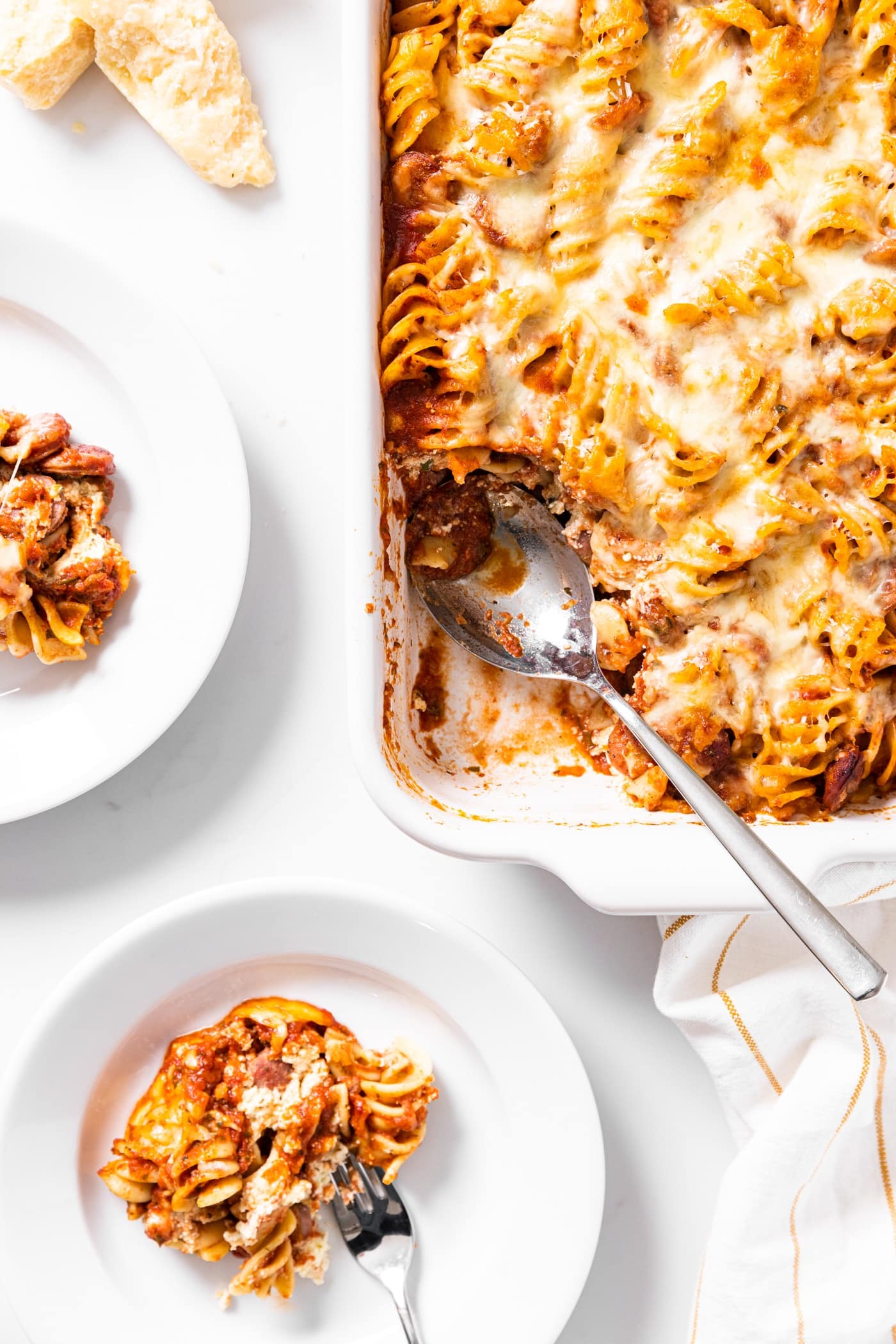 Top down view of baked rotini casserole sitting on white countertop with scoop sitting on white plate