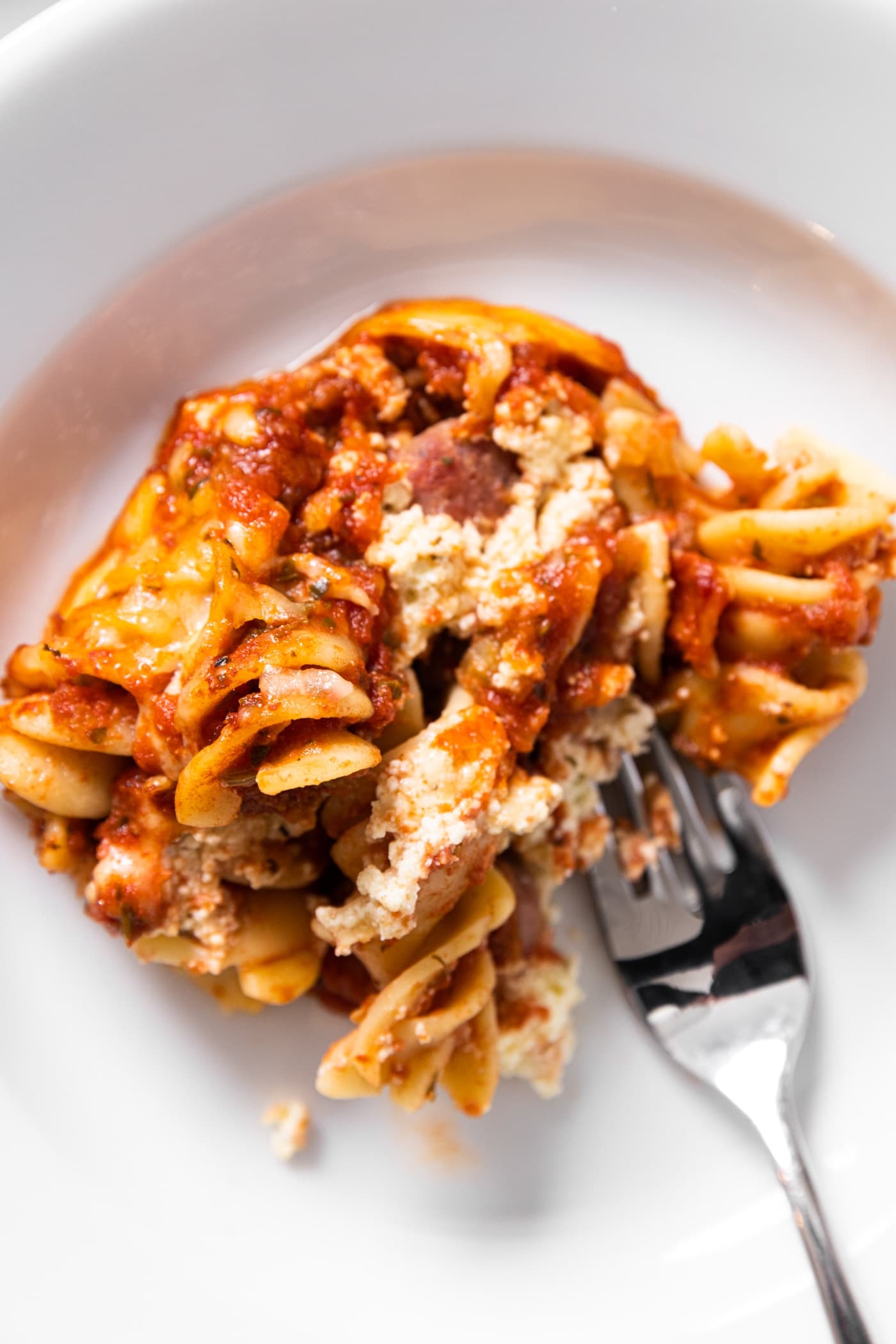 Top down view of serving of baked rotini casserole sitting on white plate with fork getting a piece