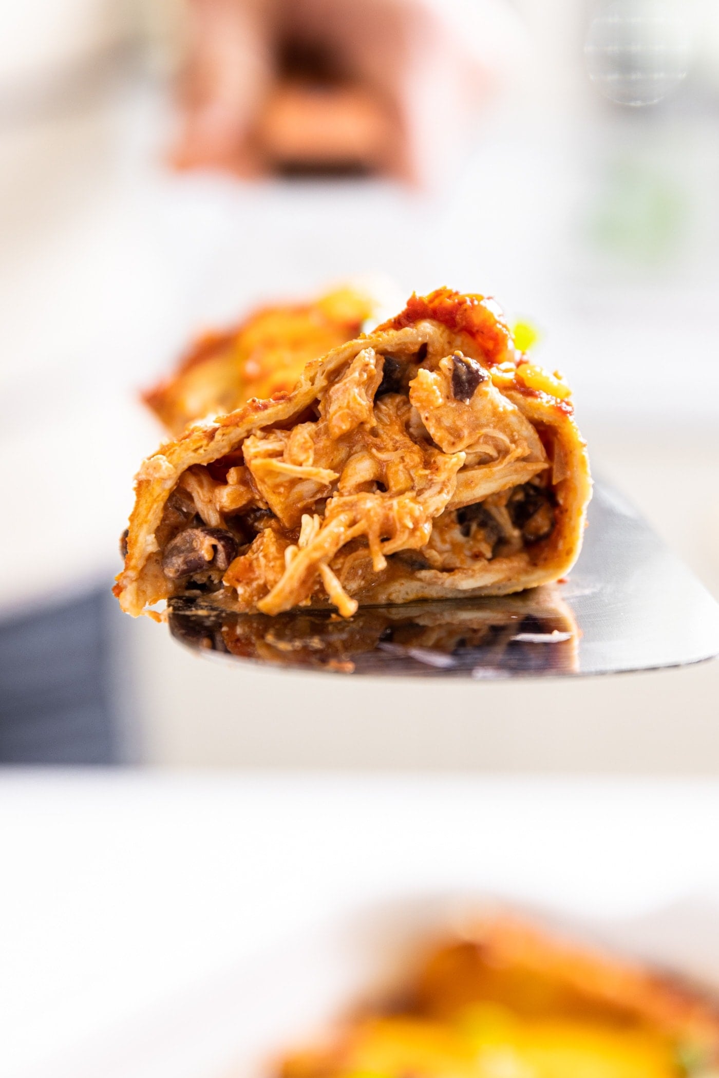 Close up side view of chicken enchilada after being cut in half and sitting on metal spatula