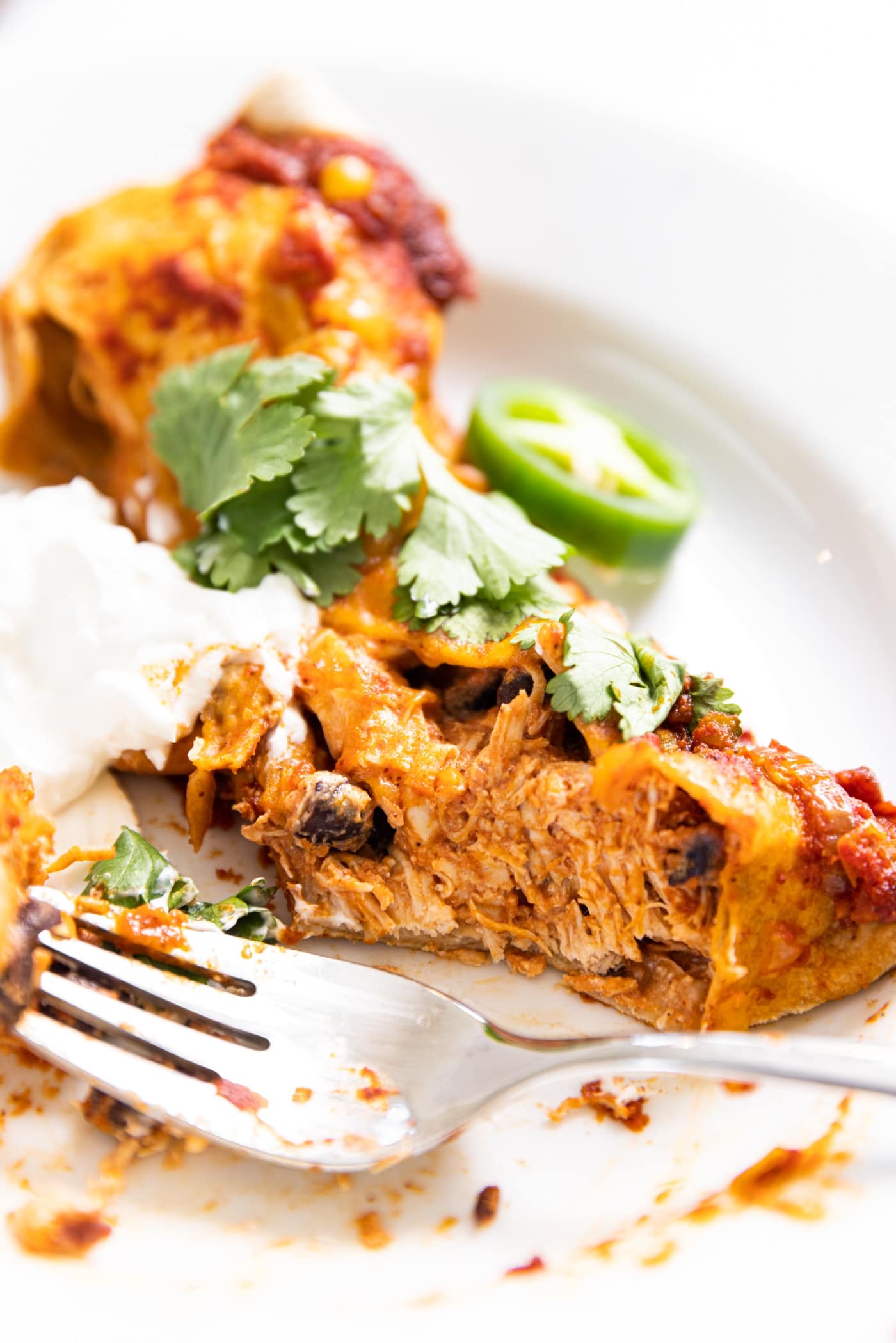 White plate with one chicken enchilada on top with fork spearing bite from taco with chicken interior showing