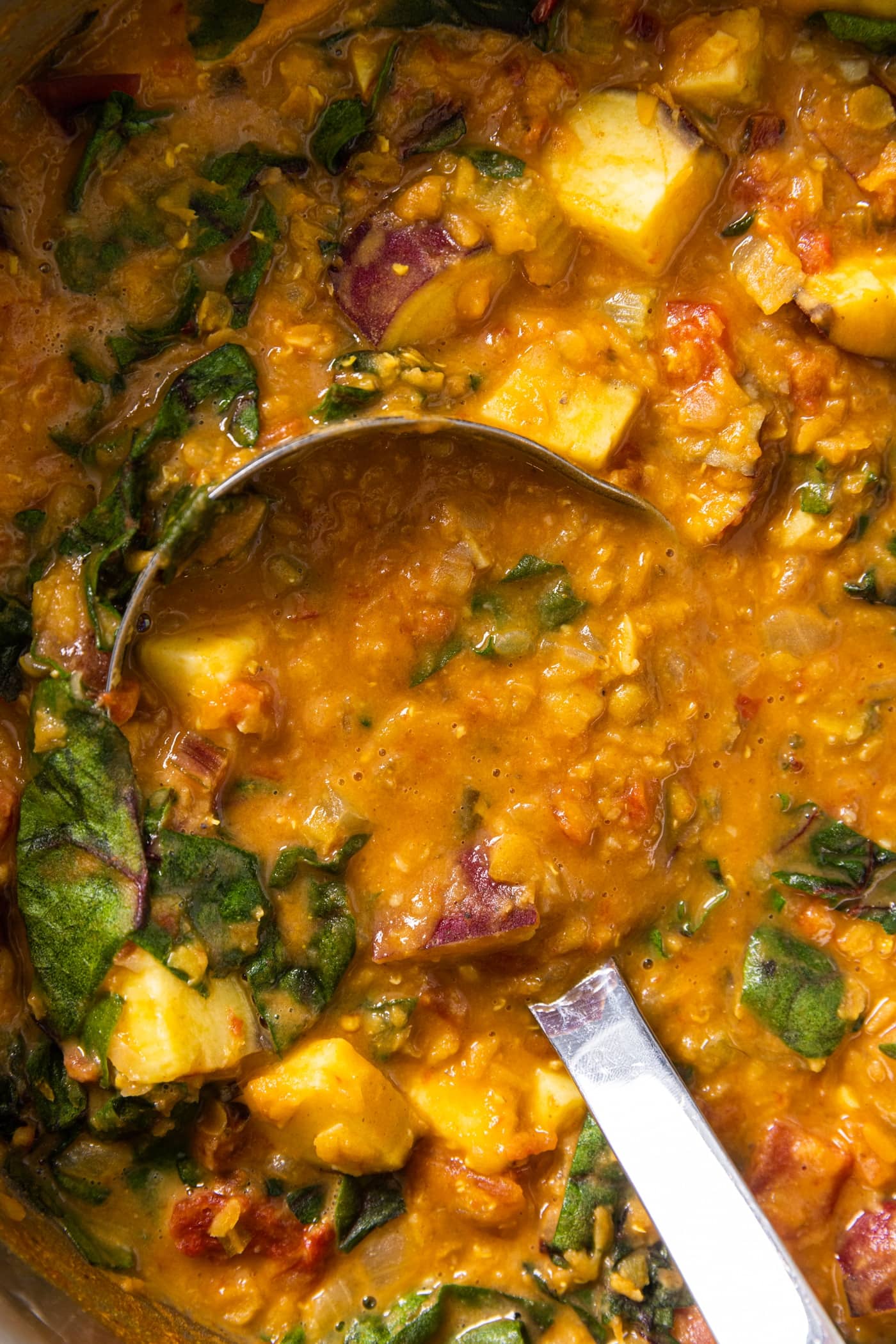Top down view of orange colored creamy curry lentil soup with chunks of sweet potato and Swiss chard