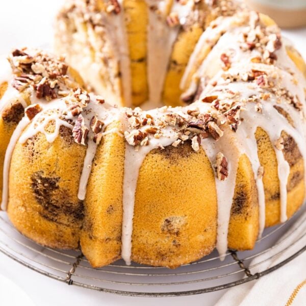 Circular coffee cake with white glaze and chopped pecans on top sitting on circular wire cooling rack on white countertop