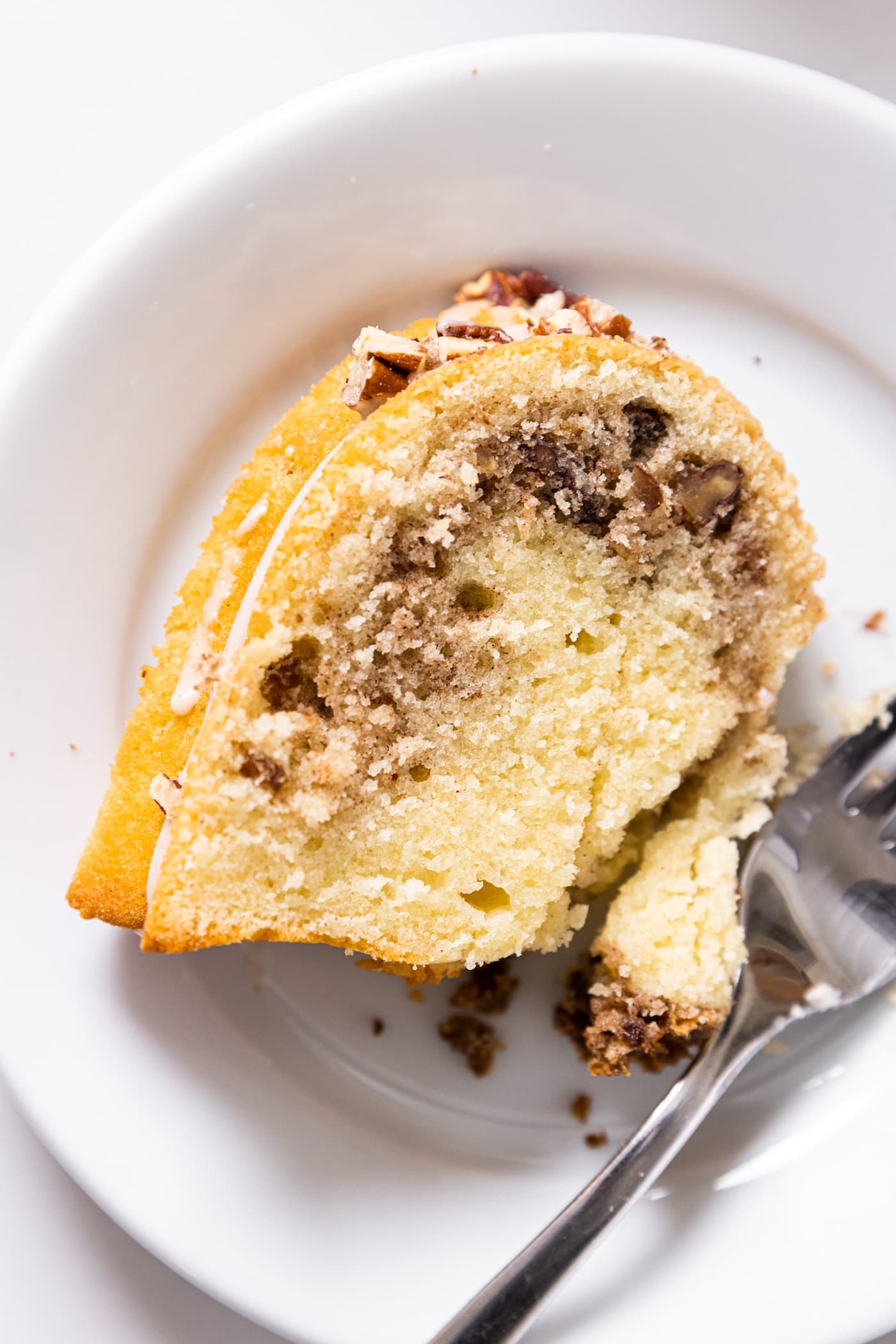 Top down view of slice of yellow colored coffee cake with cinnamon and sugar in middle sitting on white plate with fork cutting away a piece