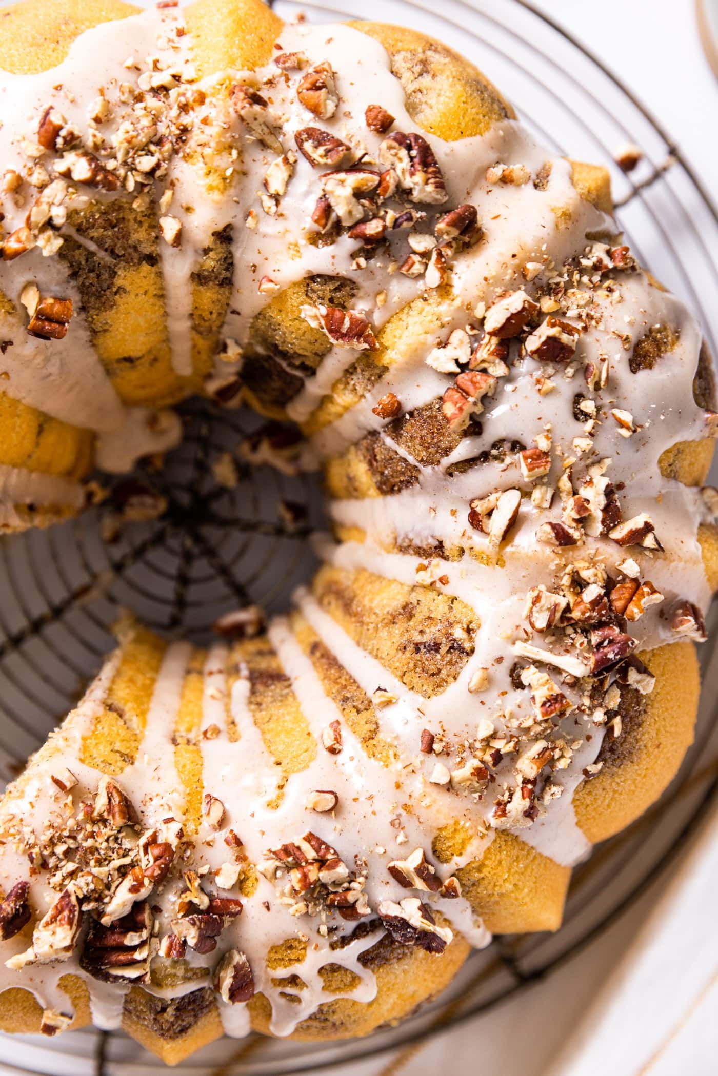 Top down view of circular Bundt coffee cake sitting on wire cooling rack with white icing and chopped pecans all over the top
