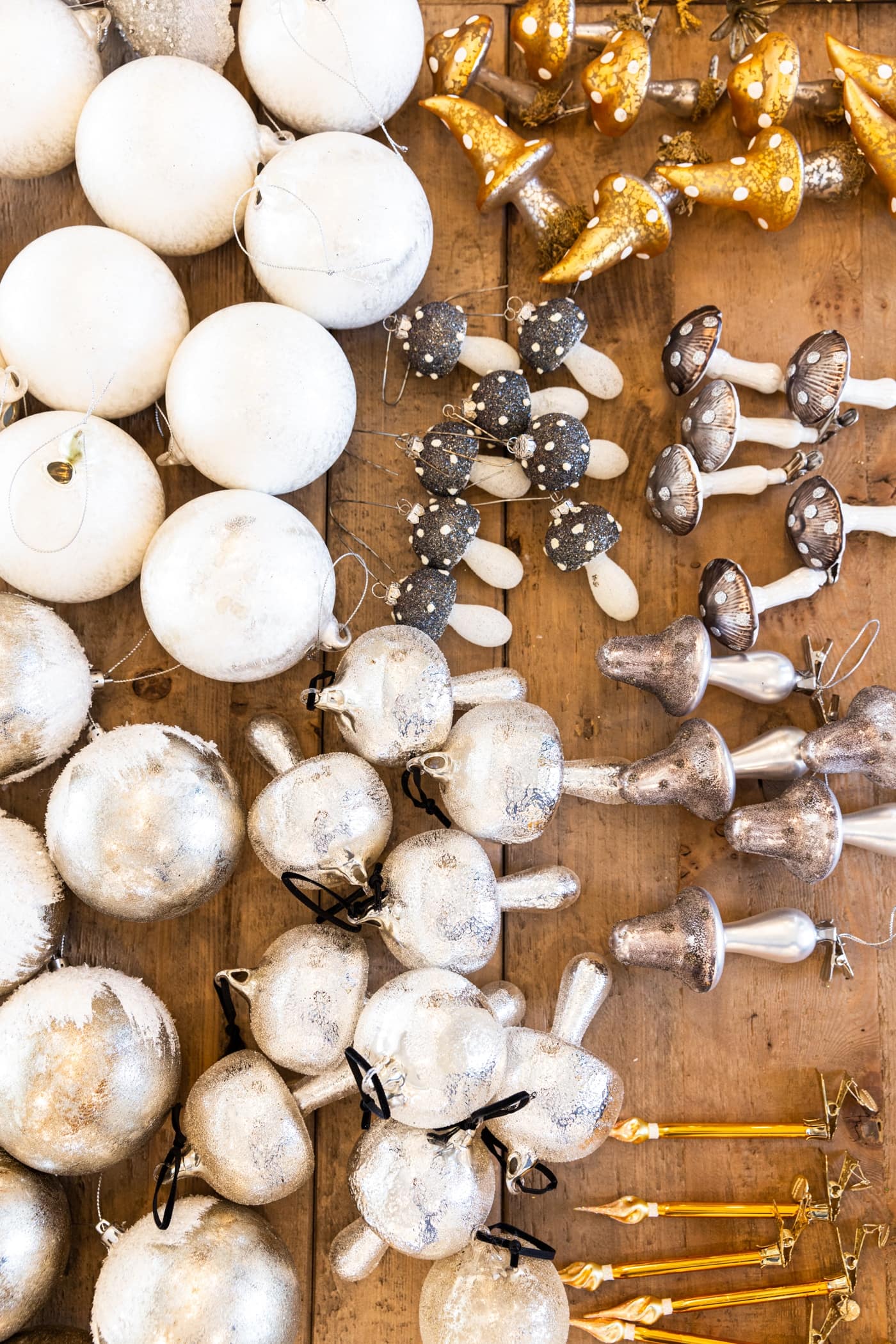 Top down view of lots of white, silver, and gold ornaments sitting on wood table, grouped by type