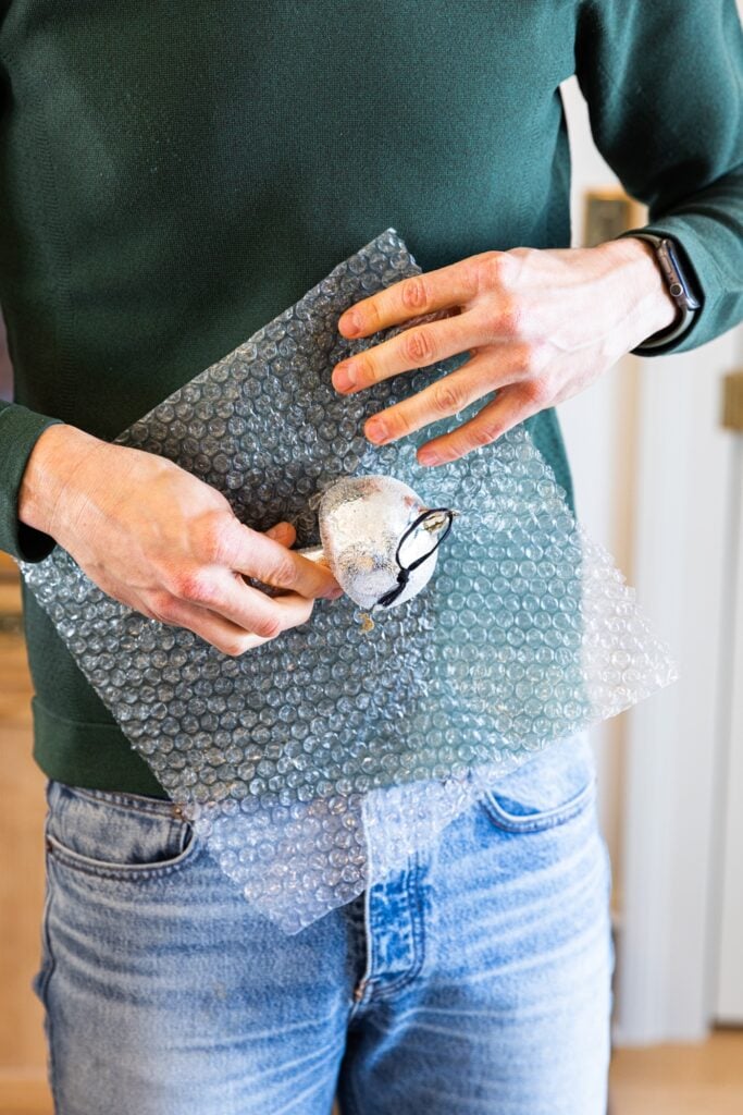 Two hands holding silver mushroom ornament with piece of bubble wrap before wrapping it