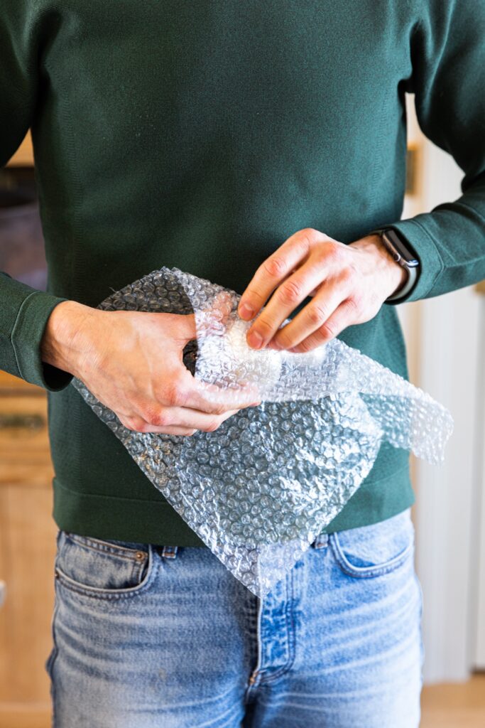 Two hands holding silver mushroom ornament with piece of bubble wrap beginning to wrap