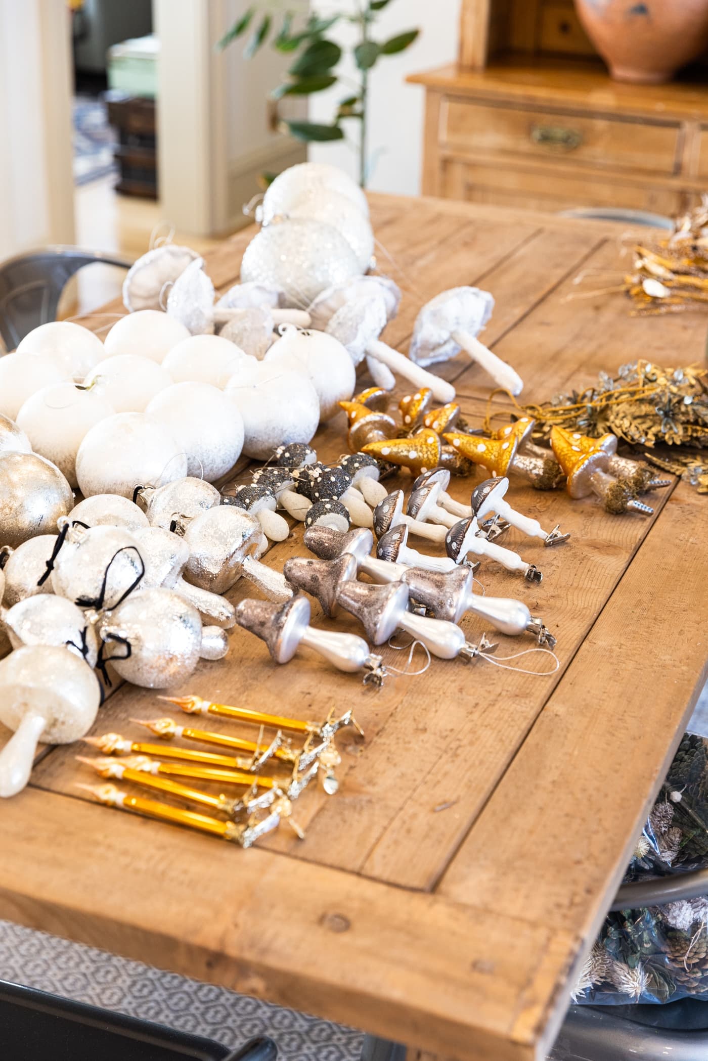 Wooden table with groups of silver, white, and gold-colored ornaments sitting all over