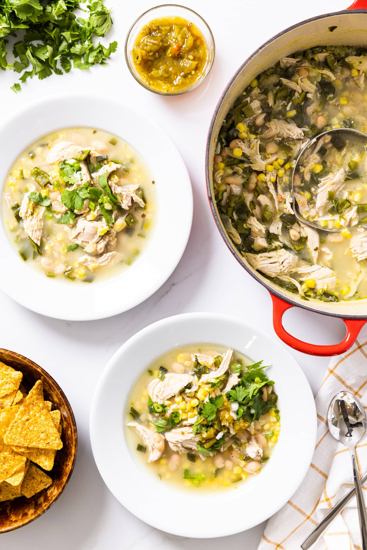 Top down view of white bowls filled with white bean chicken chili with large pot filled with remaining chili sitting on countertop